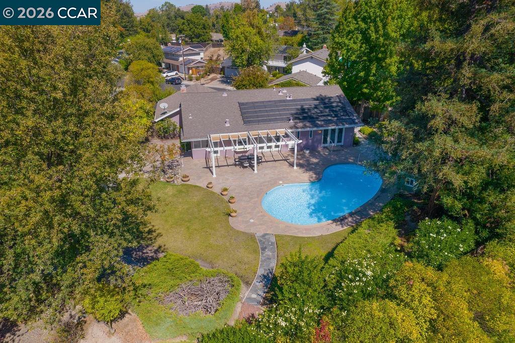 Aerial view of a home with a curved swimming pool, pergola, and rooftop solar panels.