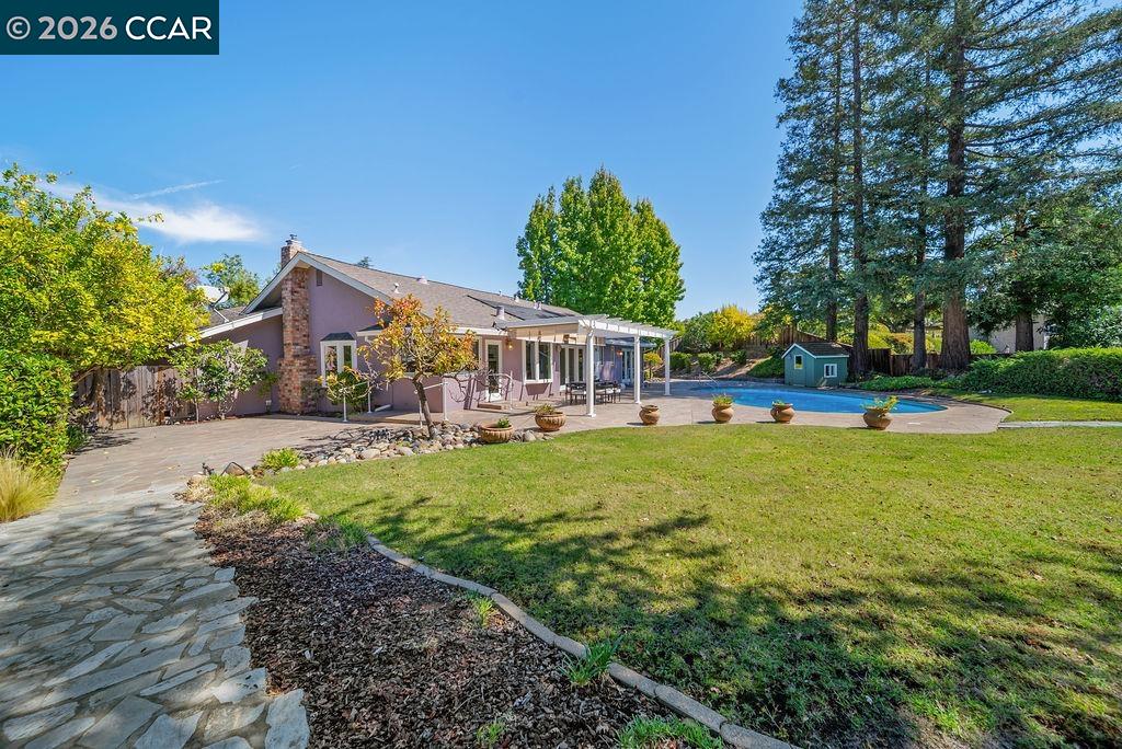 Home’s backyard with a covered patio, swimming pool, lawn, and mature trees.
