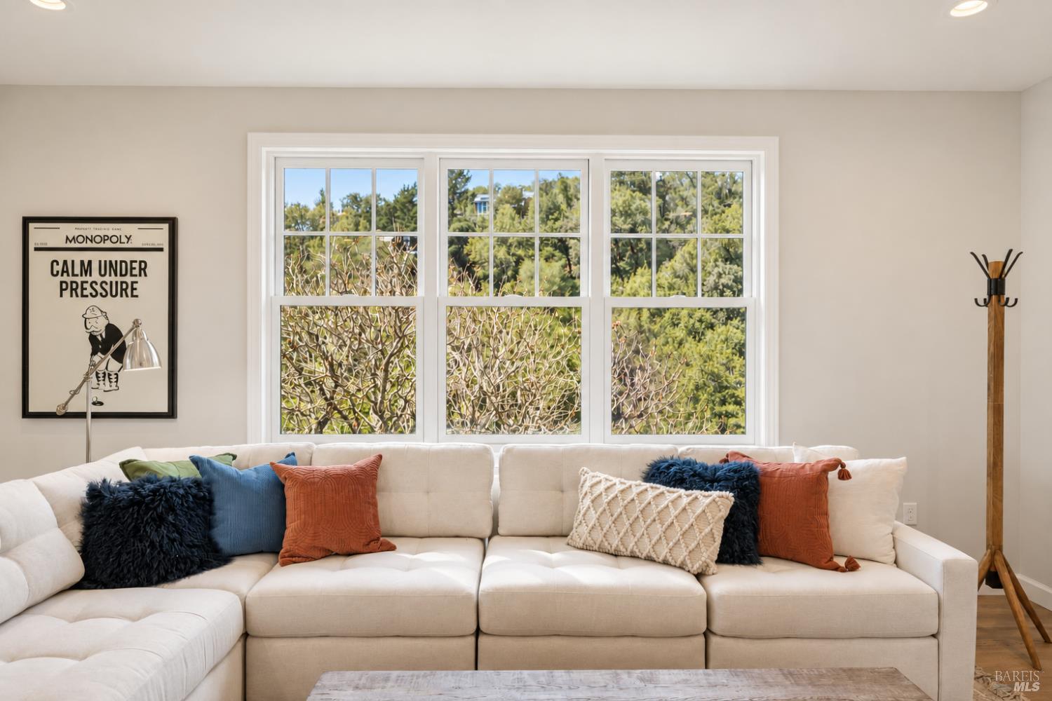 Living room with a white sectional sofa, colorful pillows, and large windows overlooking trees.
