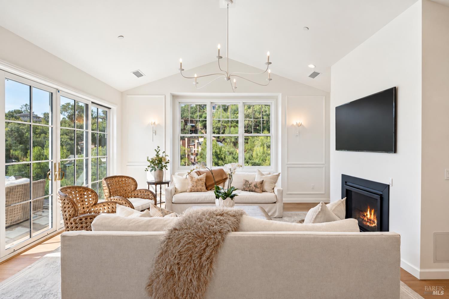 Living room with vaulted ceiling, large windows, white sofas, rattan chairs, and a fireplace.