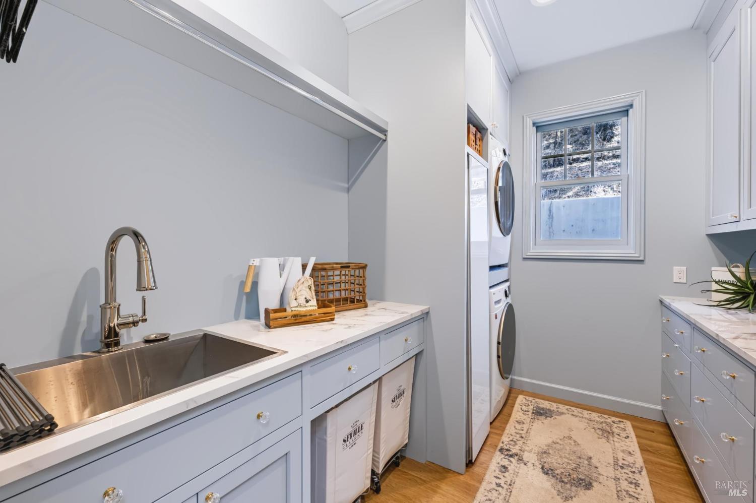Laundry room with pale blue cabinets, a stainless utility sink, and stacked washer and dryer.