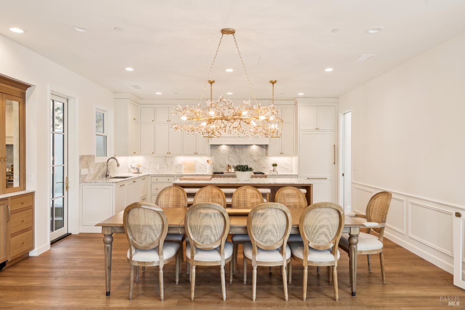 Bright kitchen and dining area with white cabinetry, marble backsplash, a large table, and a branch-style chandelier.