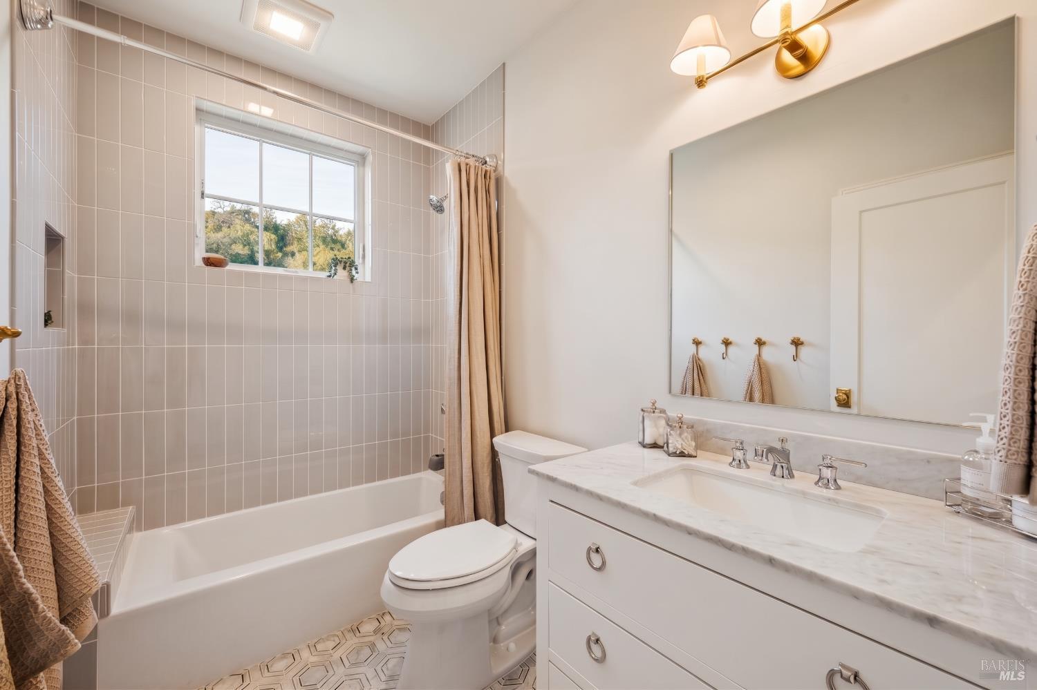 Bathroom with tiled tub and shower, marble-look vanity, large mirror, and window.
