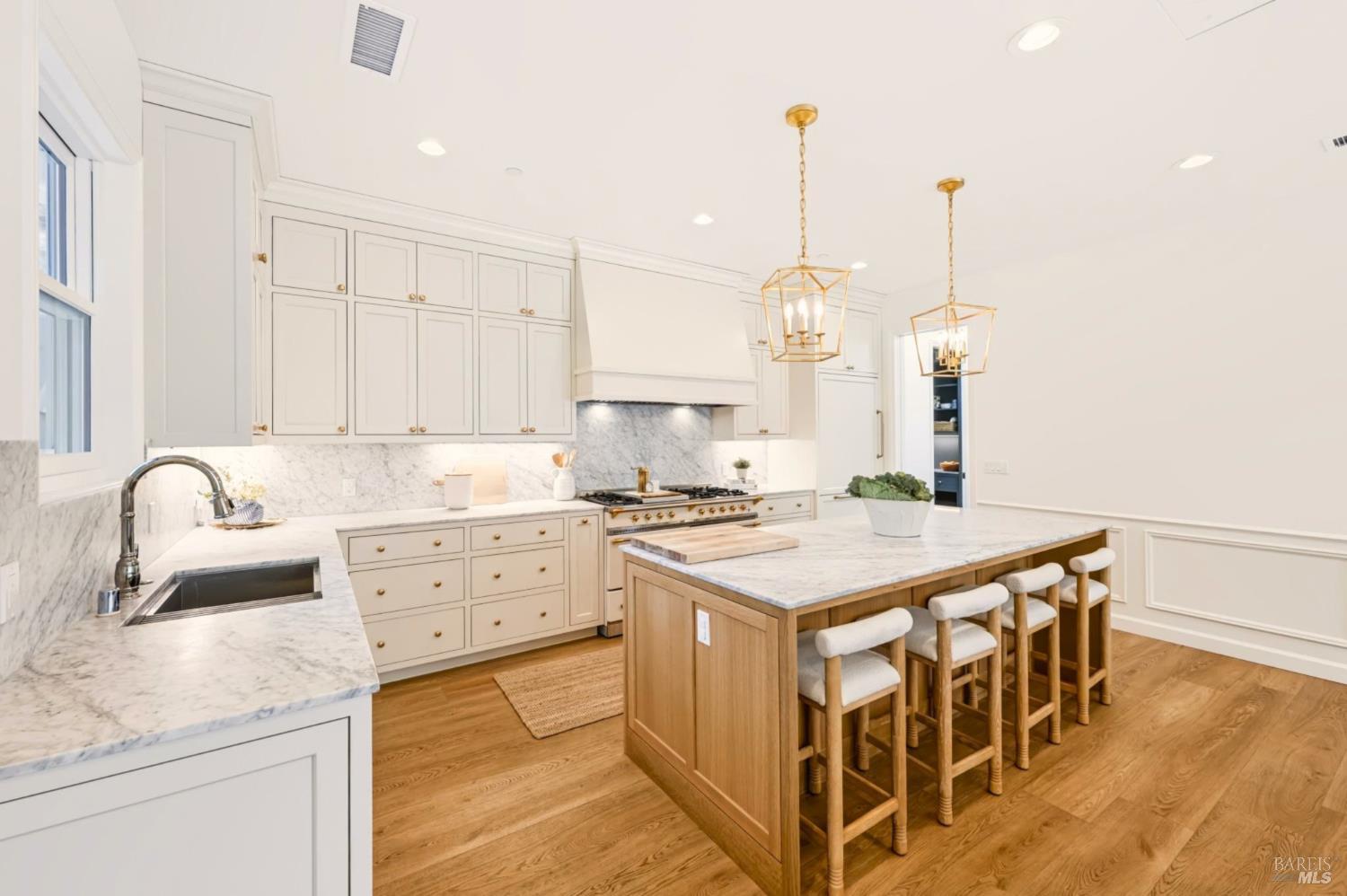Bright kitchen with a marble-topped island, white cabinetry, brass pendants, and hardwood floors.