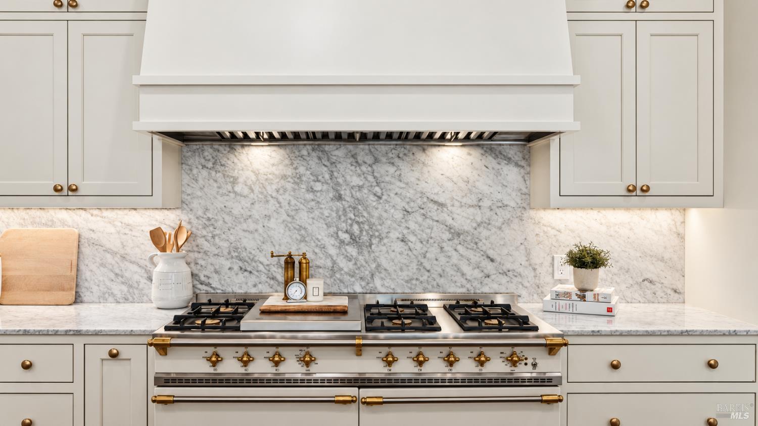 Kitchen with a large brass-trimmed range, marble backsplash, and white cabinetry.