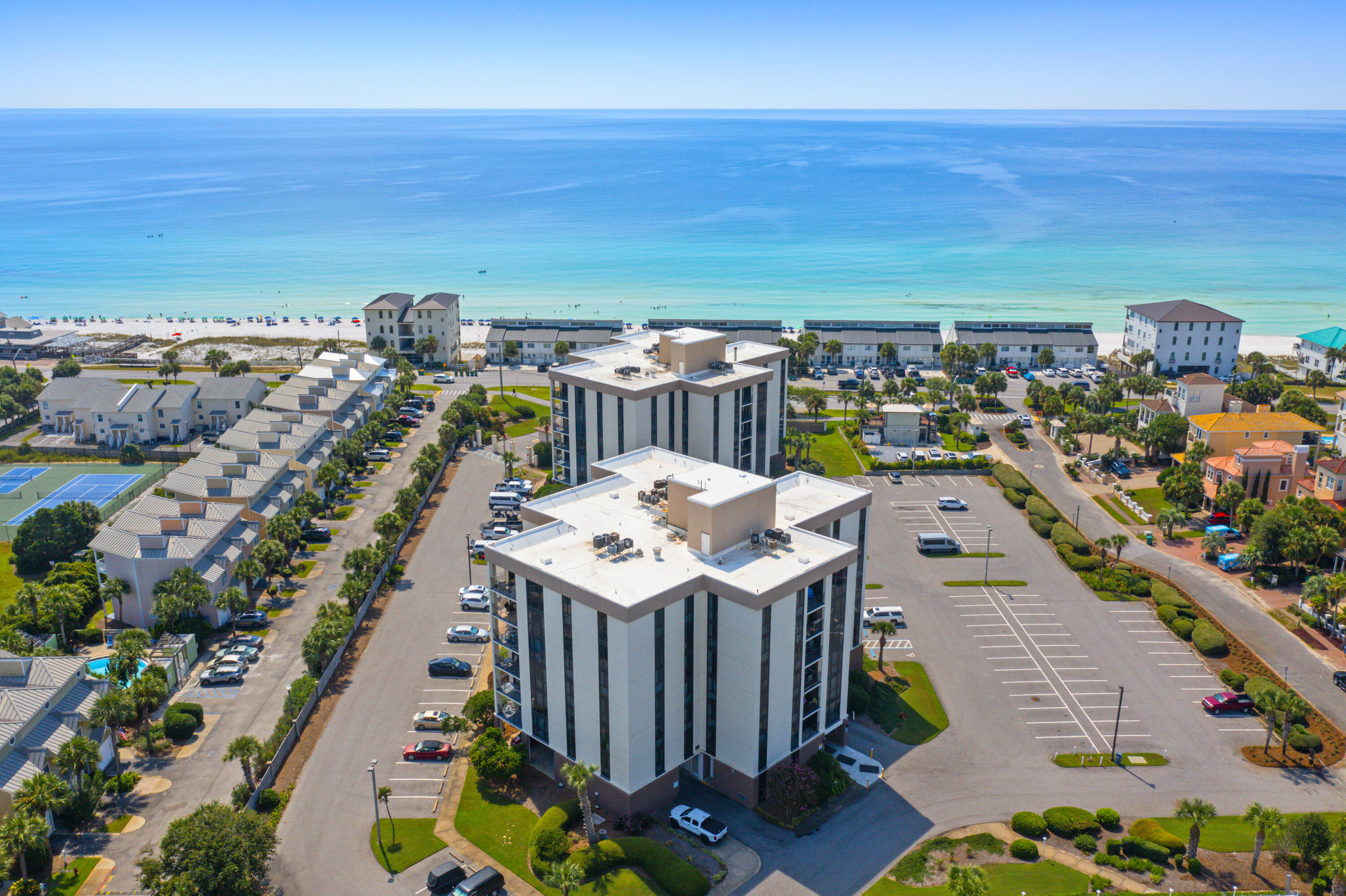 Aerial view of coastal condominium towers beside a beach and turquoise Gulf waters.