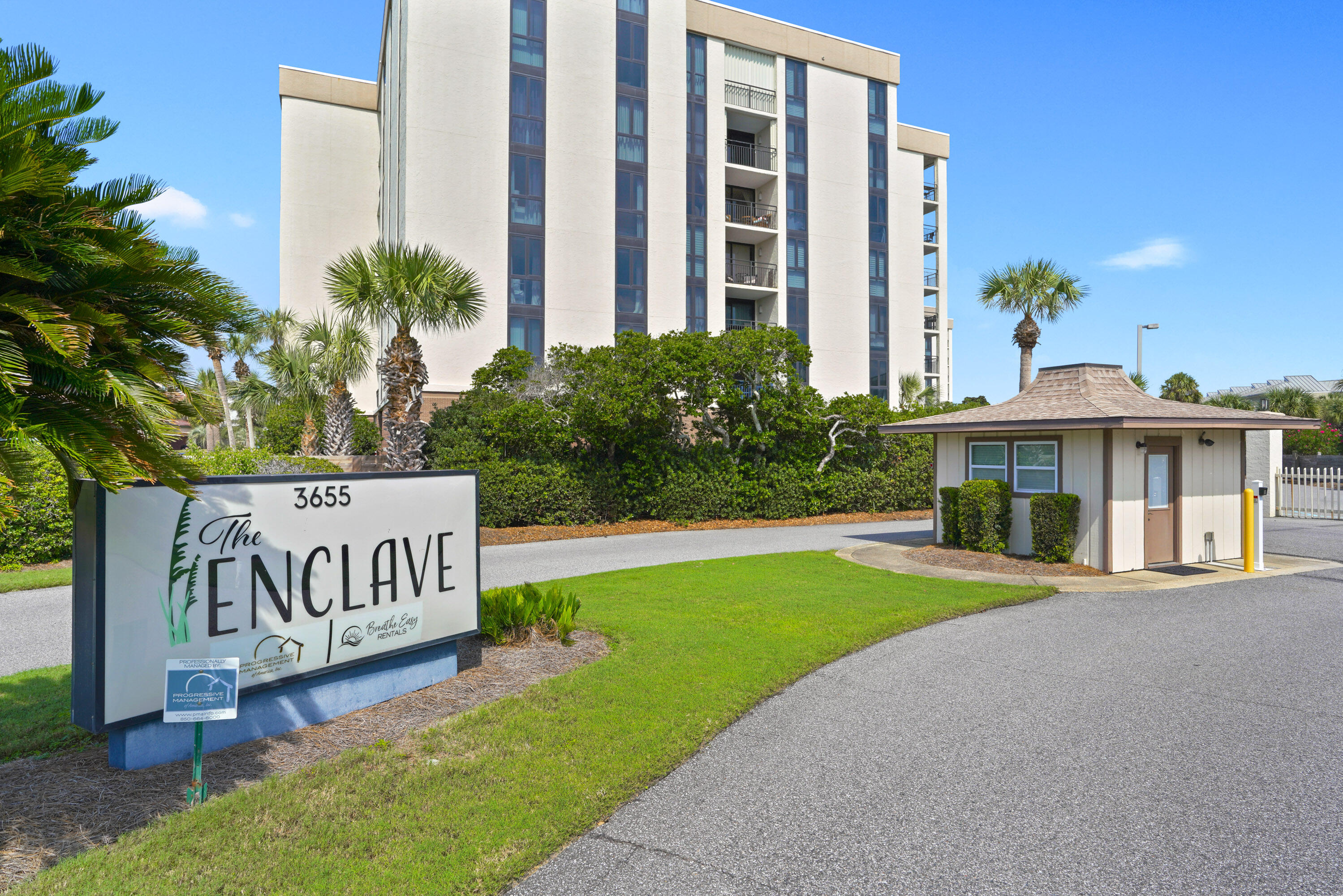 The Enclave condominium building behind its entrance sign, with palm trees and a guardhouse.
