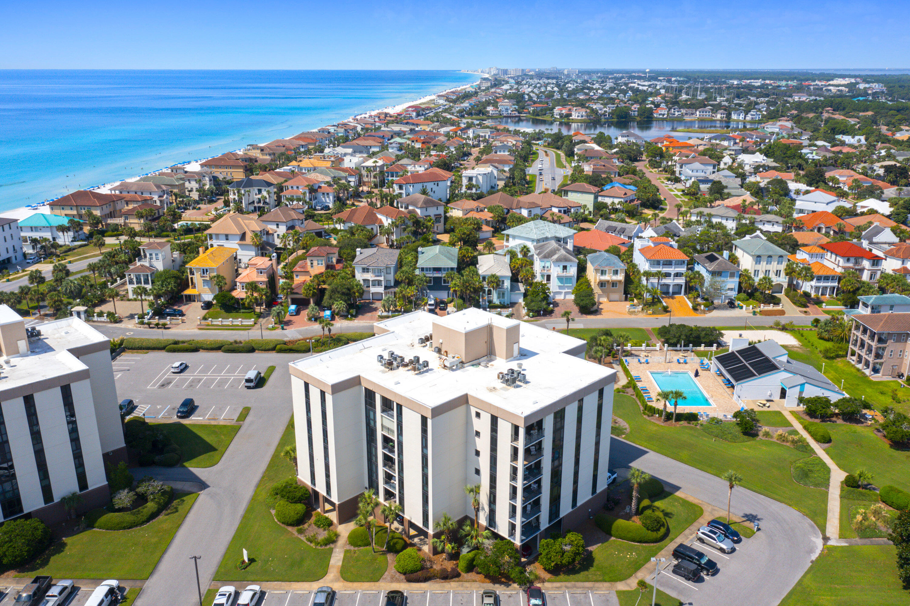 Aerial view of a beachfront condominium complex, pool, and coastal homes along the turquoise Gulf shoreline.