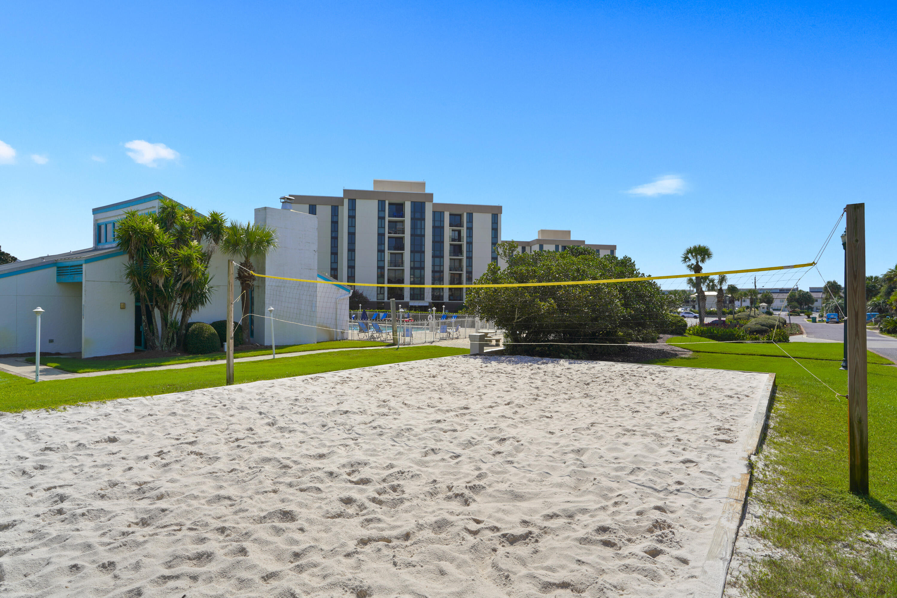 Sand volleyball court with a yellow net in front of a condominium building and pool area.