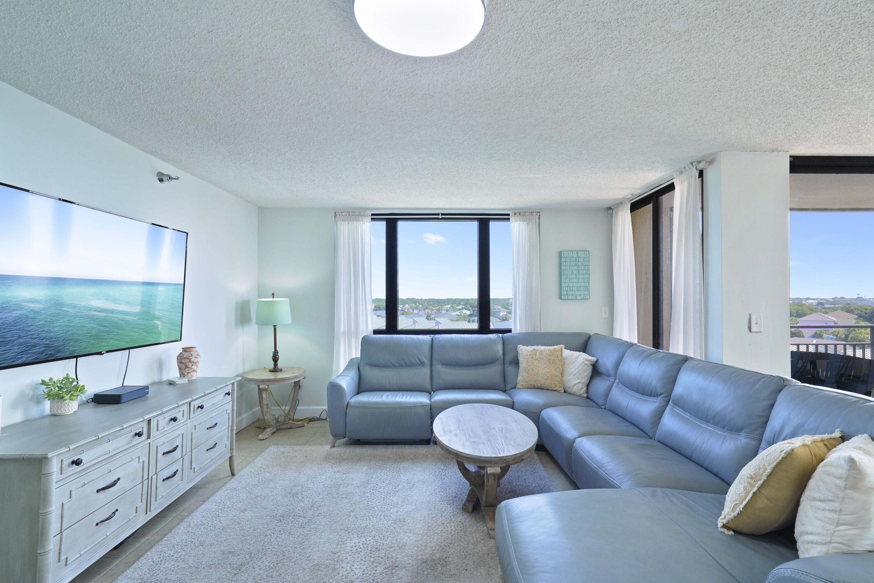 Living room with a blue sectional sofa, oval coffee table, and windows overlooking nearby homes.