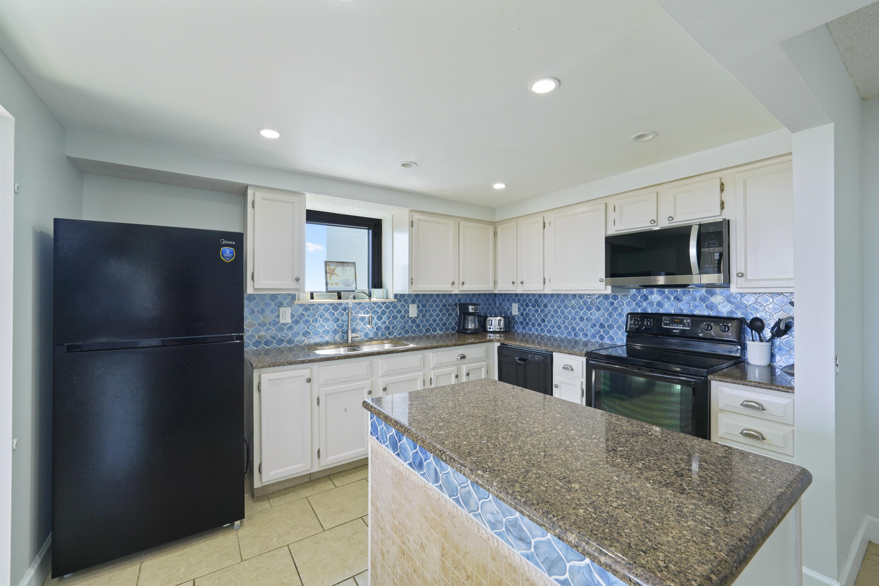 Condominium kitchen with a blue tile backsplash and a large granite island.