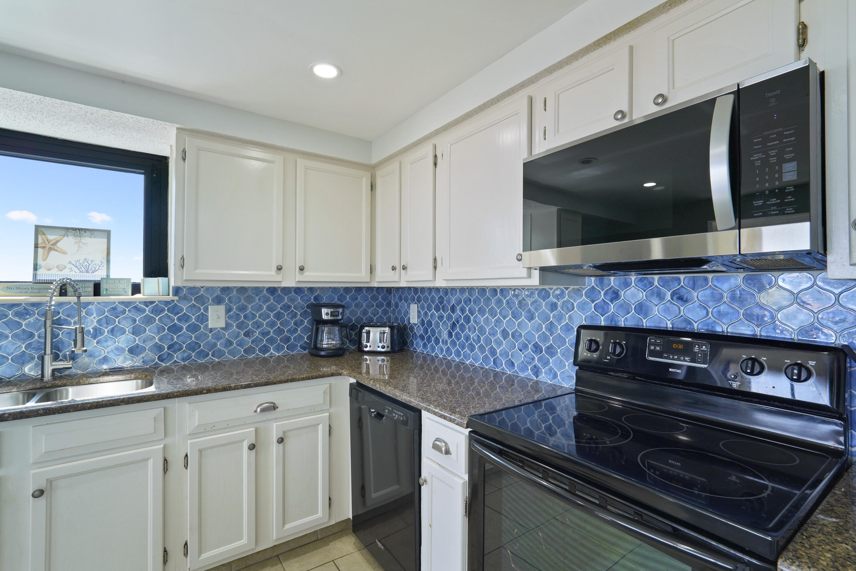Kitchen with white cabinets, vivid blue tile backsplash, dark countertops, and black electric range.
