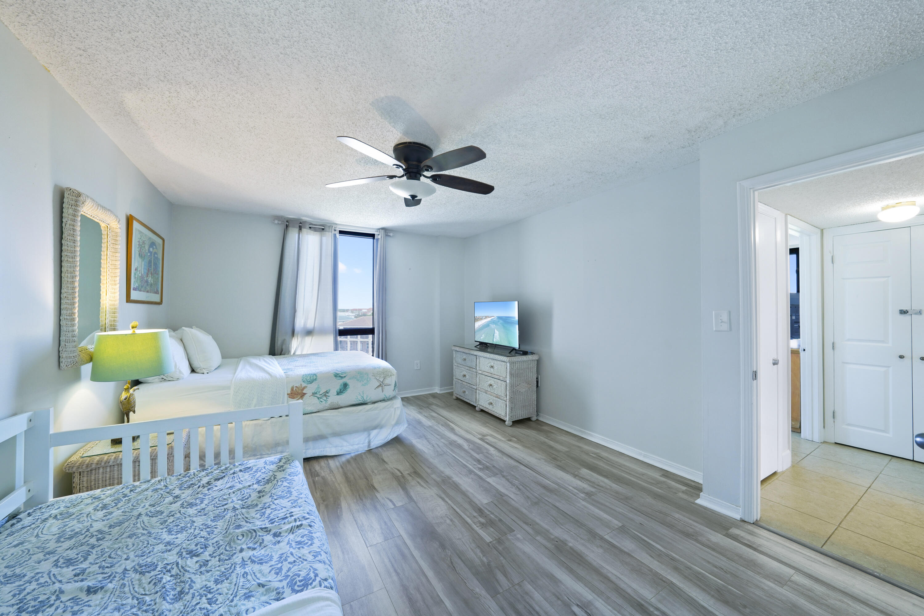 Bedroom with two beds, a ceiling fan, and a television on a woven dresser.