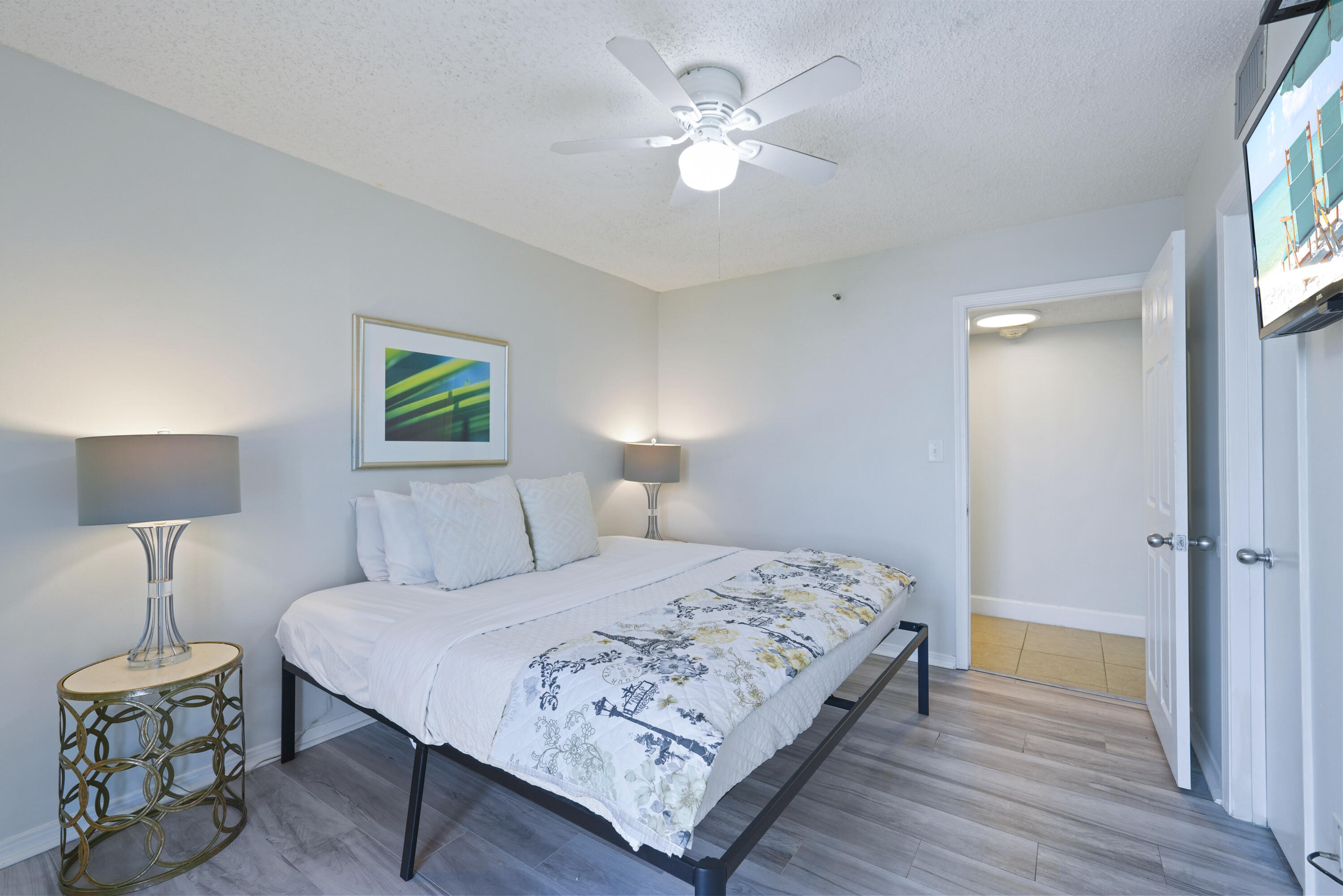 Furnished bedroom with a white bed, patterned quilt, ceiling fan, and open doorway.