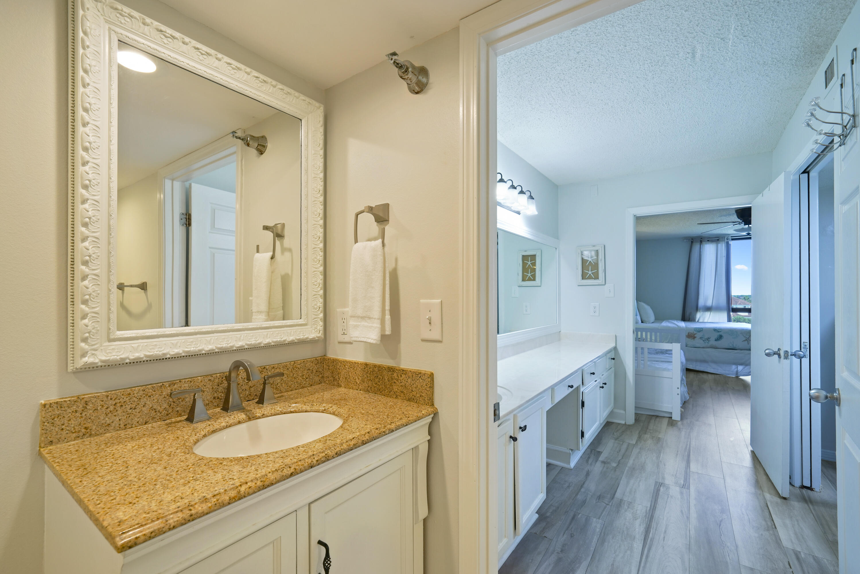 Bathroom vanity with speckled granite countertop and ornate mirror, looking through to an adjoining bedroom.