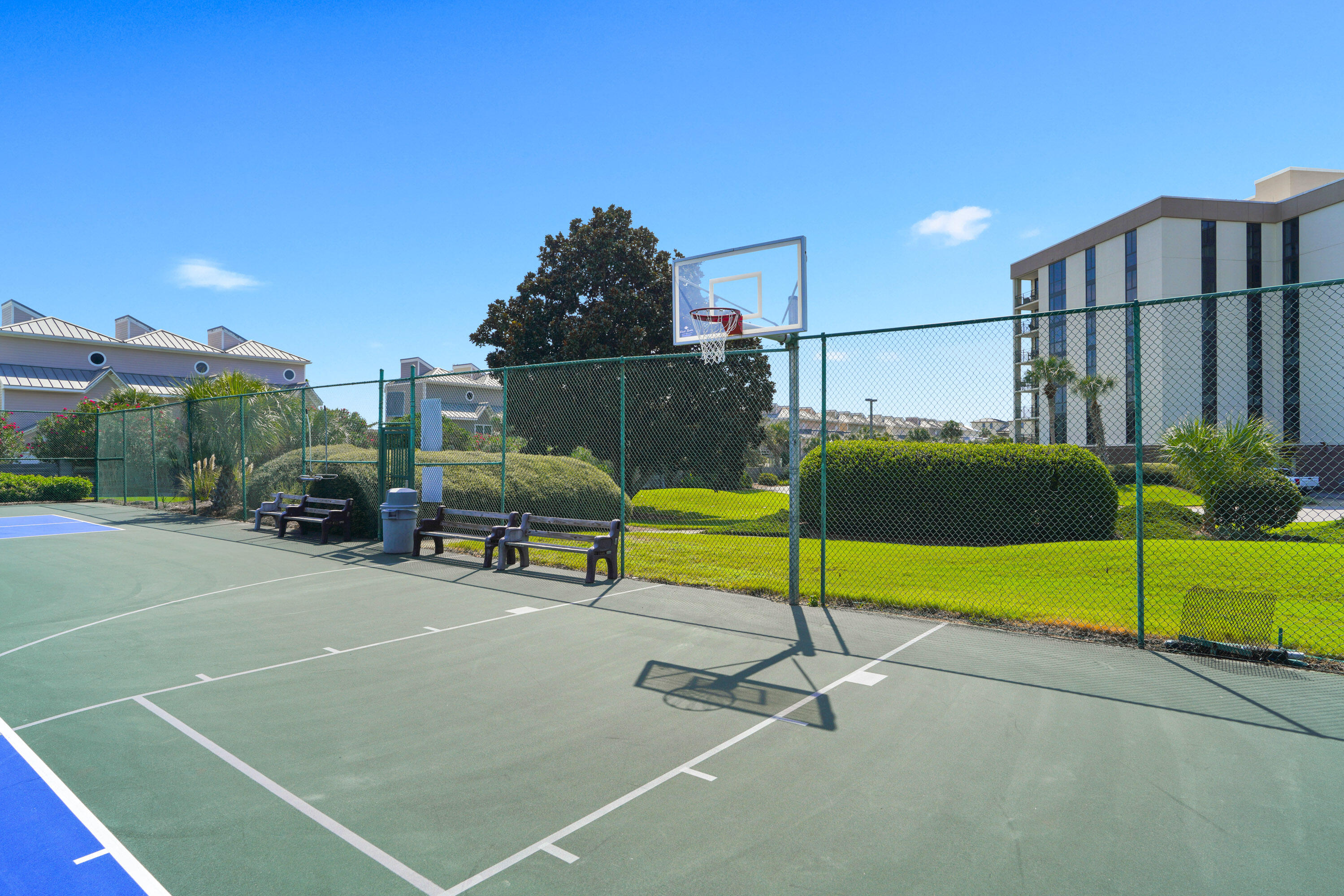 Outdoor court with a basketball hoop, chain-link fencing, and benches beside a condominium building.