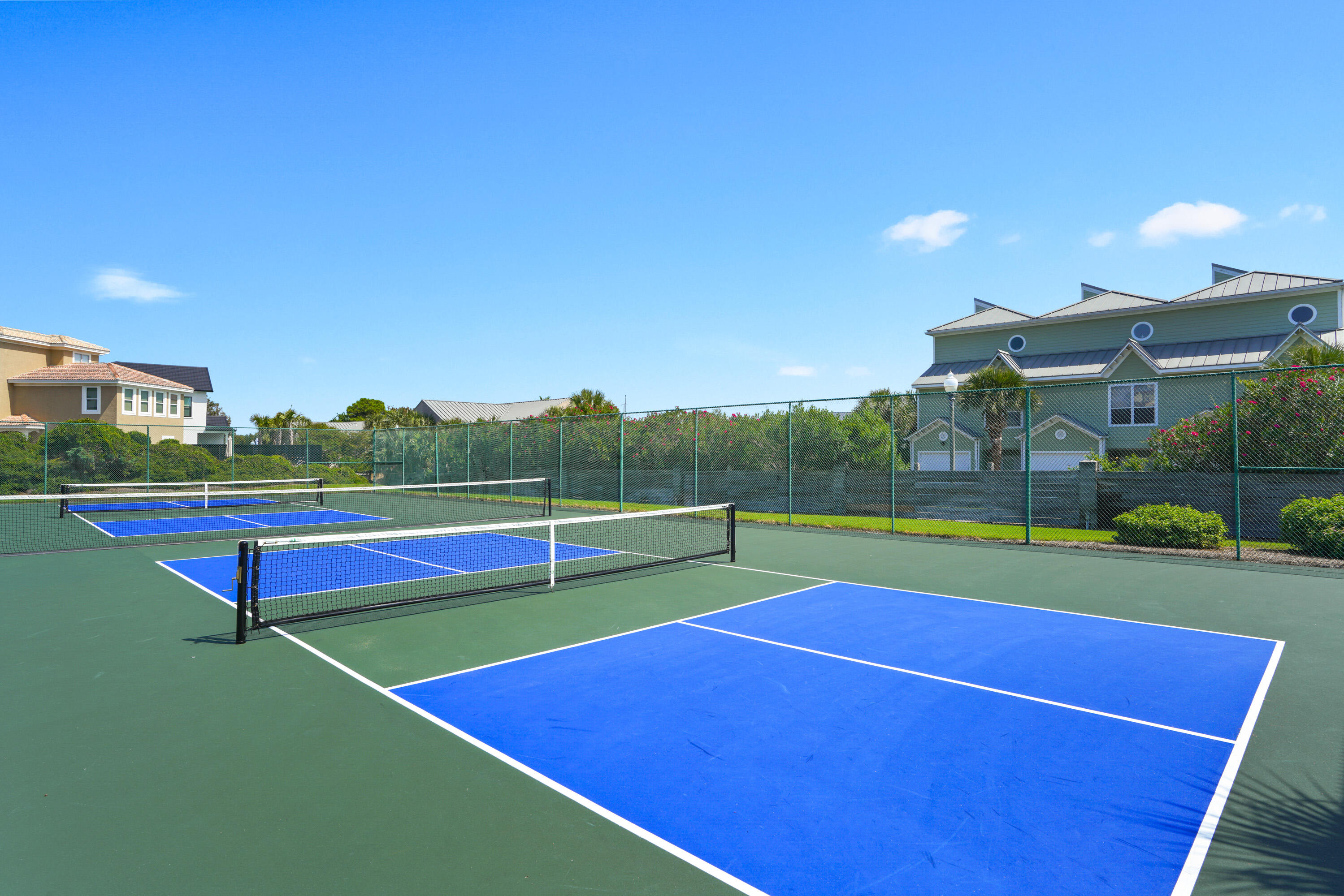 Fenced blue-and-green pickleball courts with nets, with residential buildings behind them.
