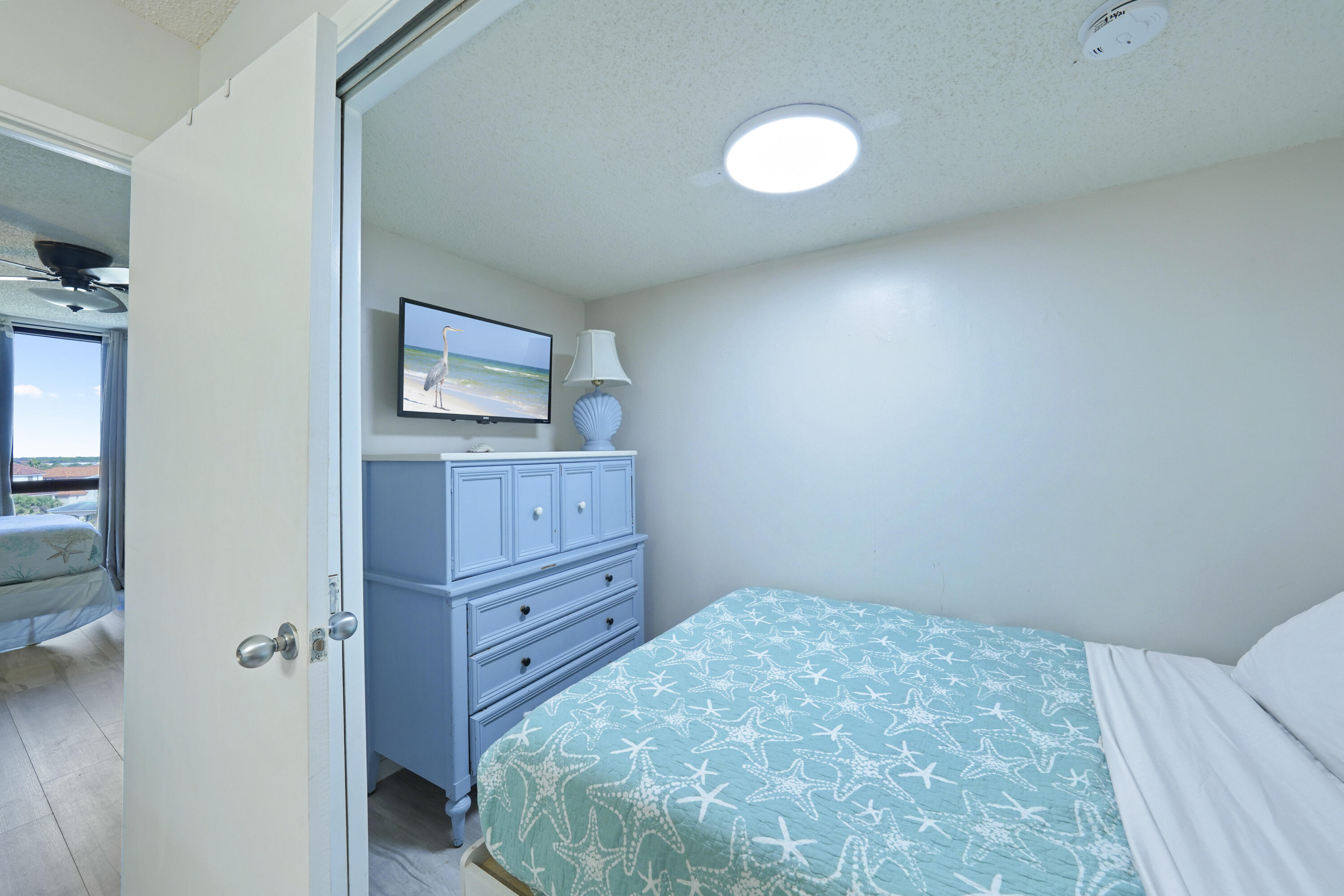 Bedroom with a turquoise starfish bedspread and blue dresser; doorway opens to a second bedroom.