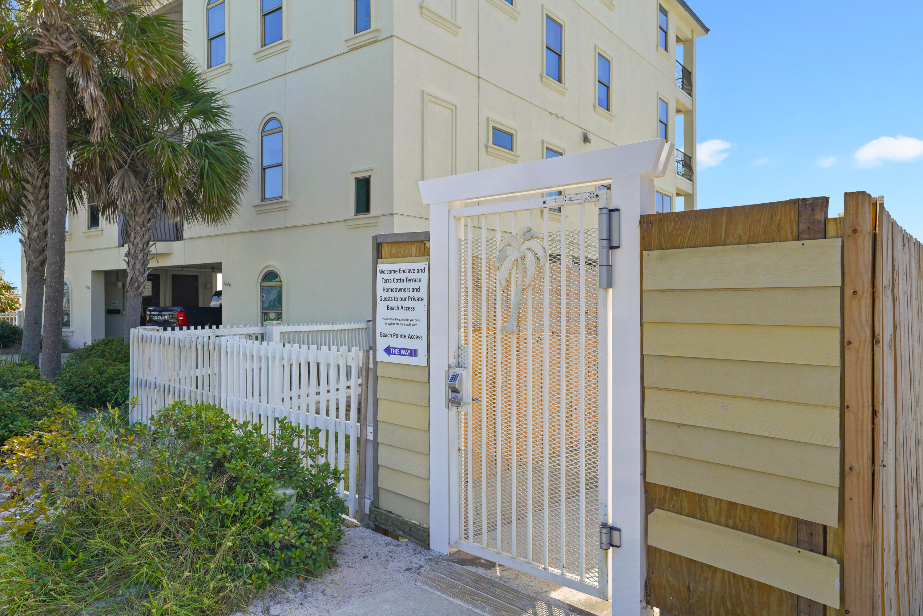 Condominium exterior beside a gated private beach access walkway with palm trees and a Beach Pointe Access sign.