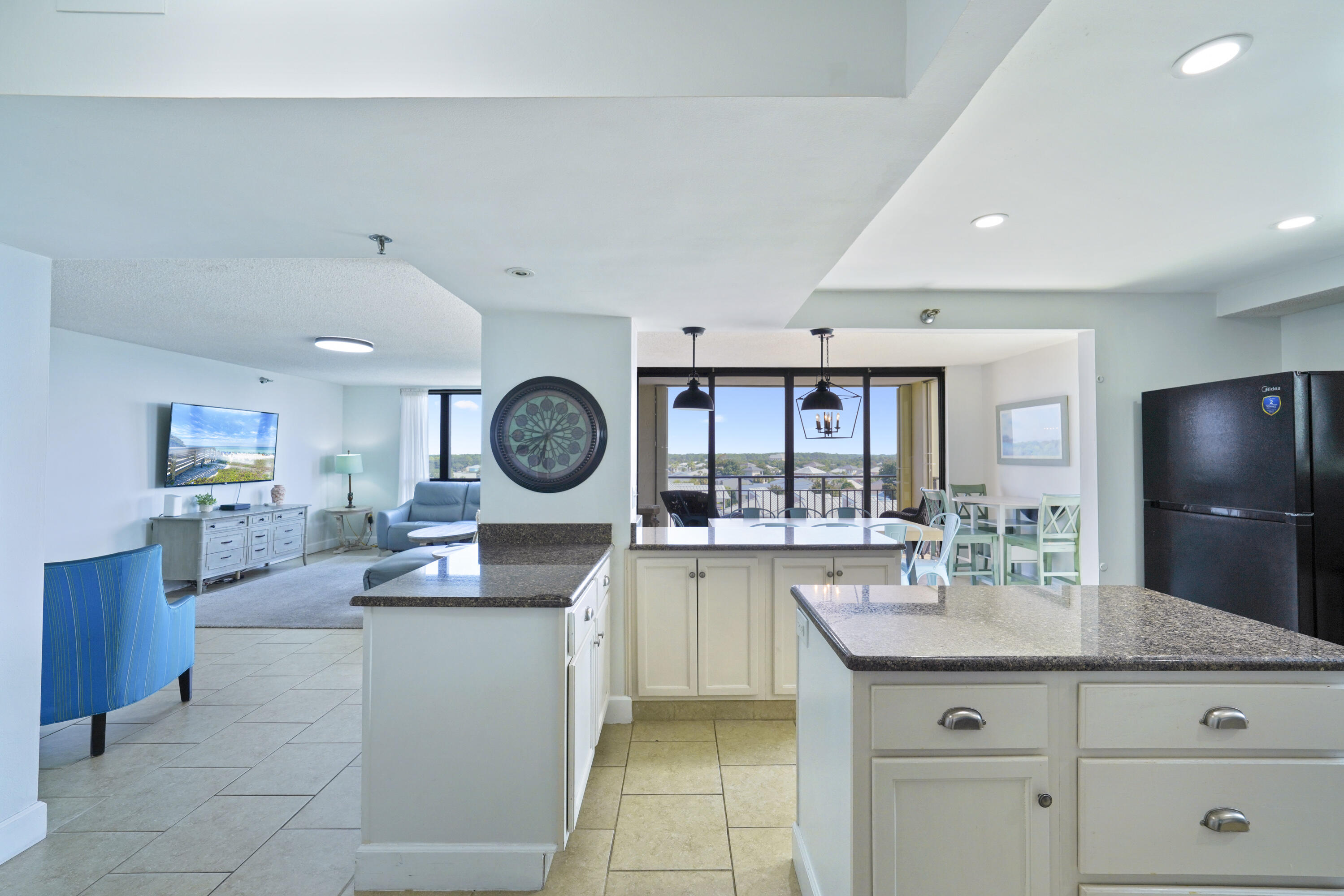 Open-plan condo kitchen with granite counters, adjoining living and dining areas, and balcony doors.