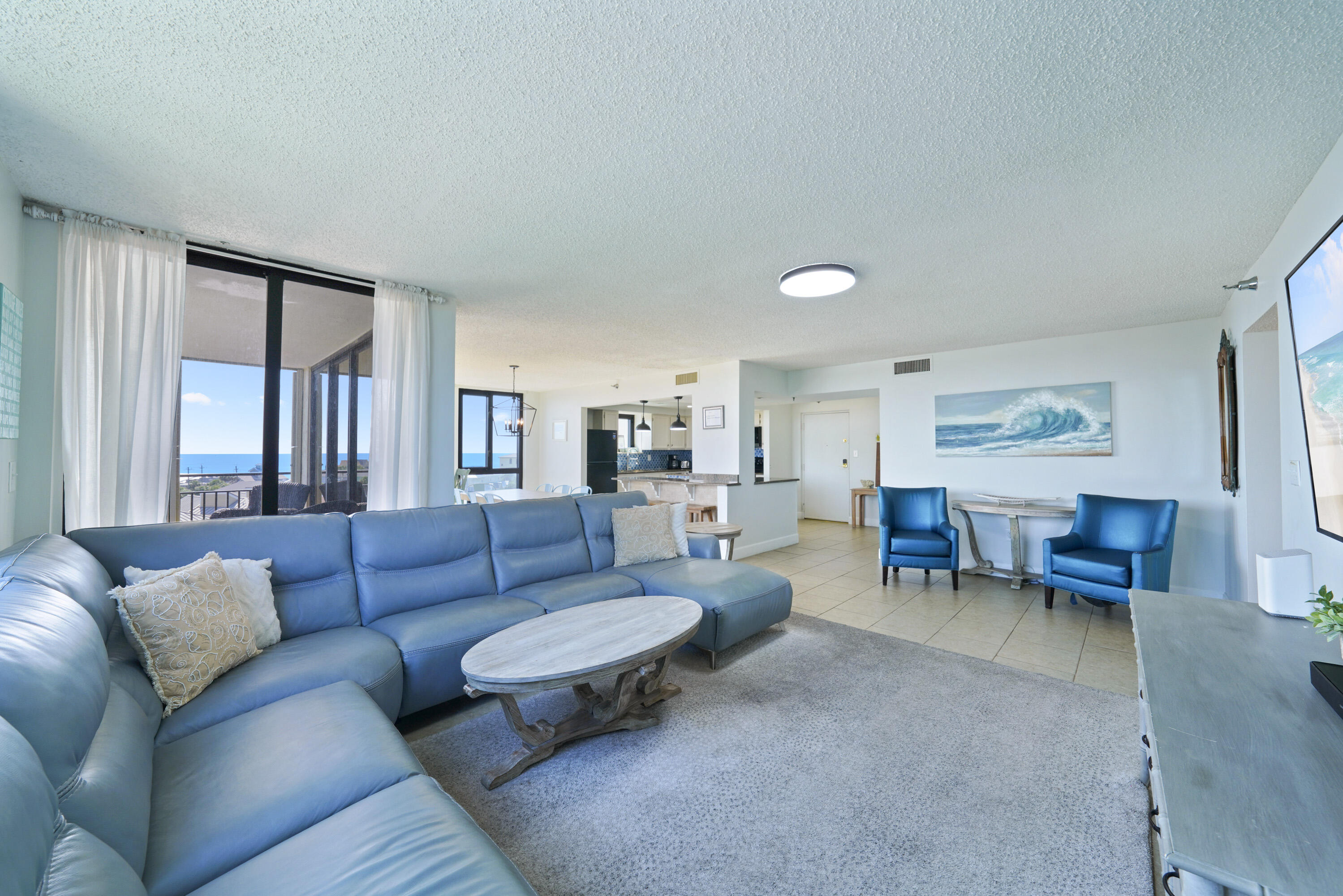 Coastal condo living room with blue seating and water visible through sliding glass doors.