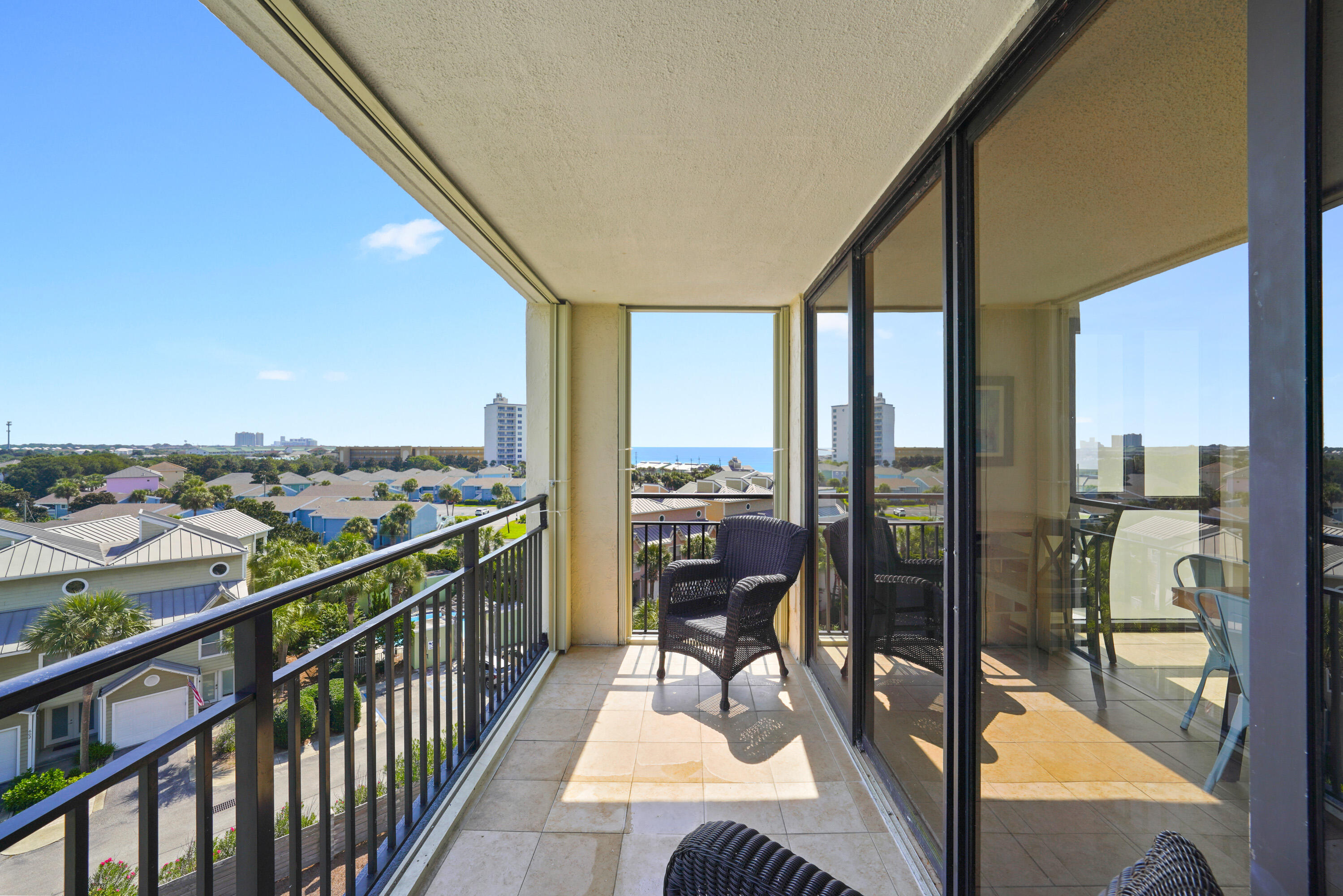 Condo balcony with wicker chairs overlooking nearby homes and a strip of blue water