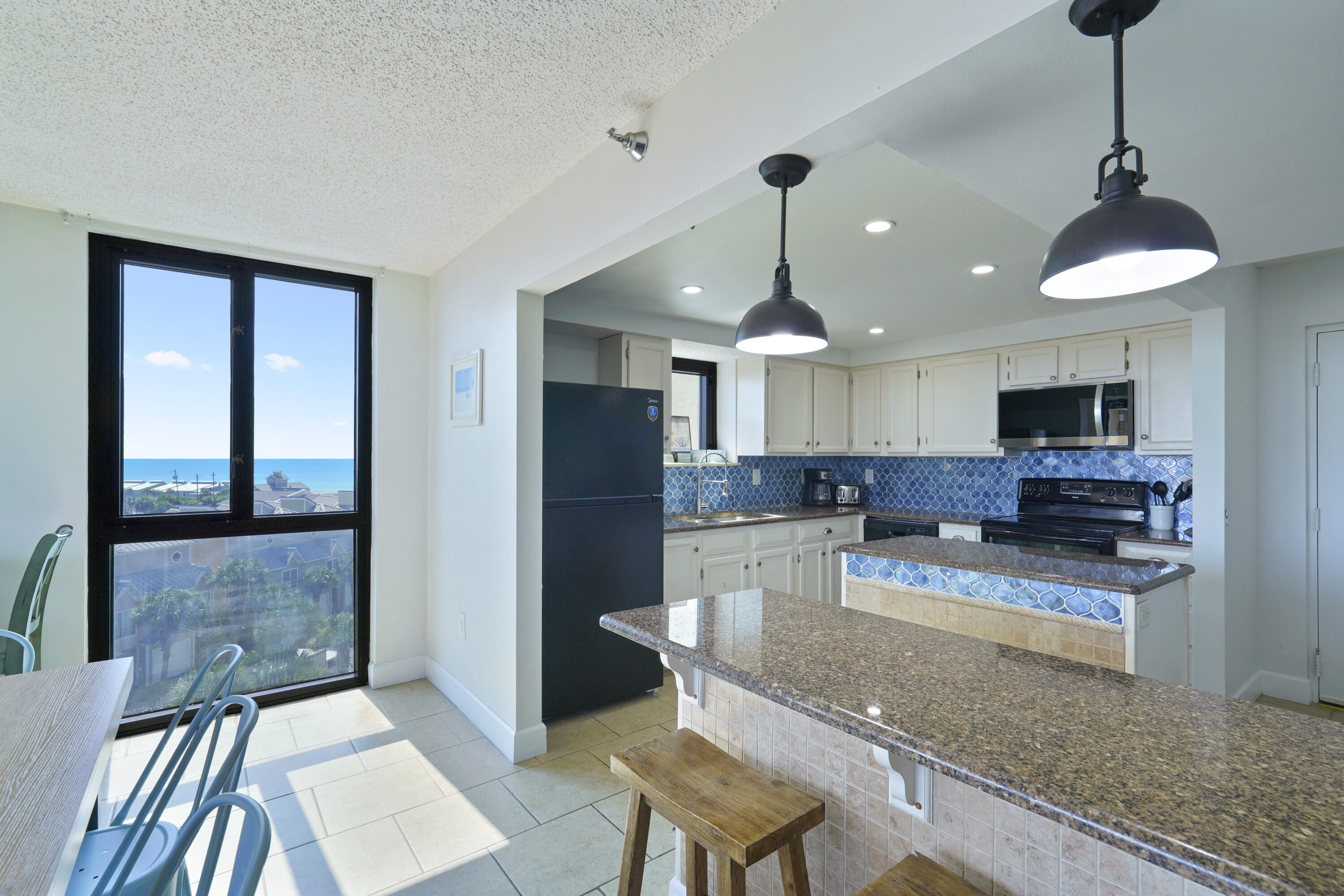 Condo kitchen with blue tile backsplash, granite breakfast bar, and a window overlooking the Gulf.