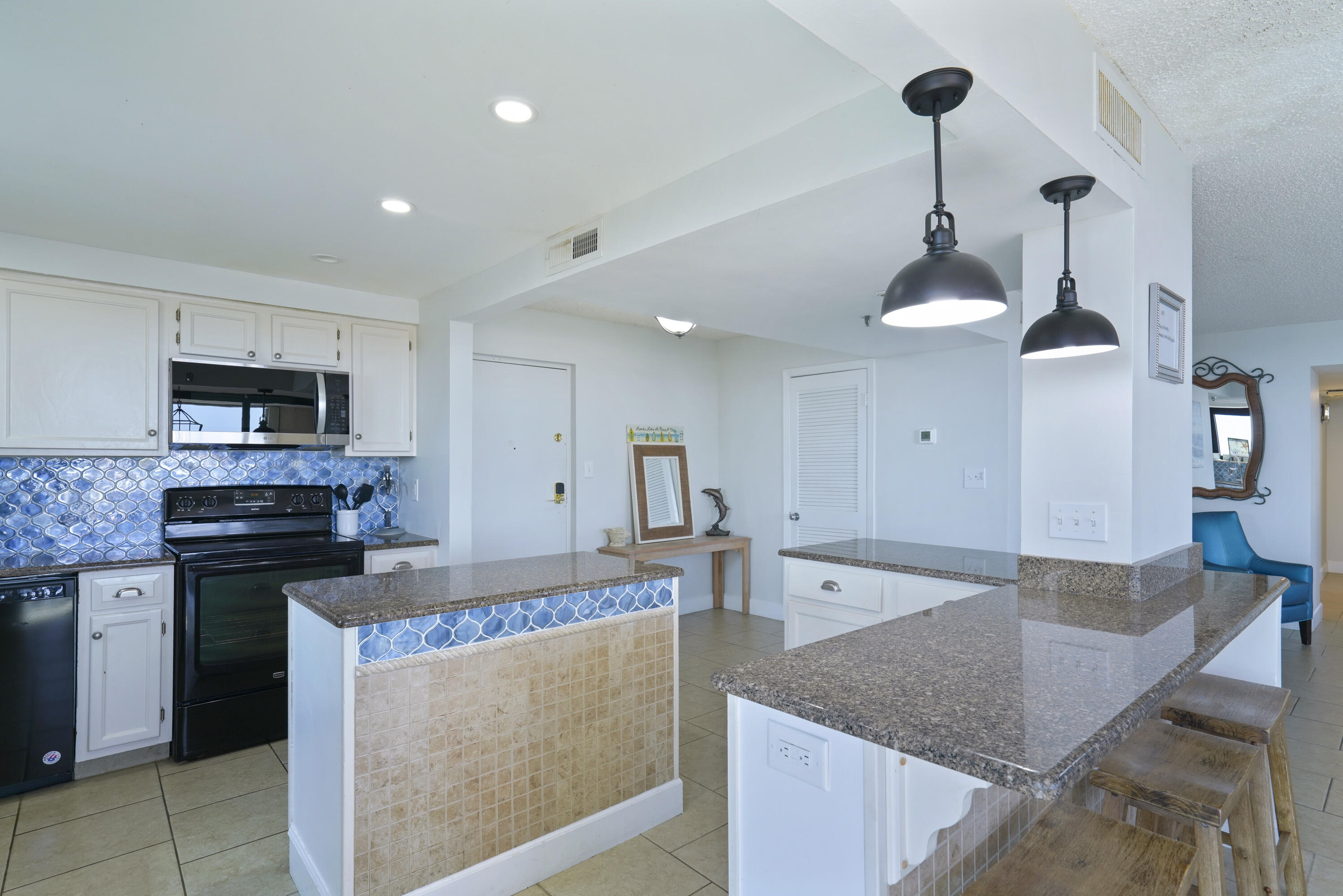 Condo kitchen with blue patterned backsplash, granite island, black appliances, and wooden bar stools.