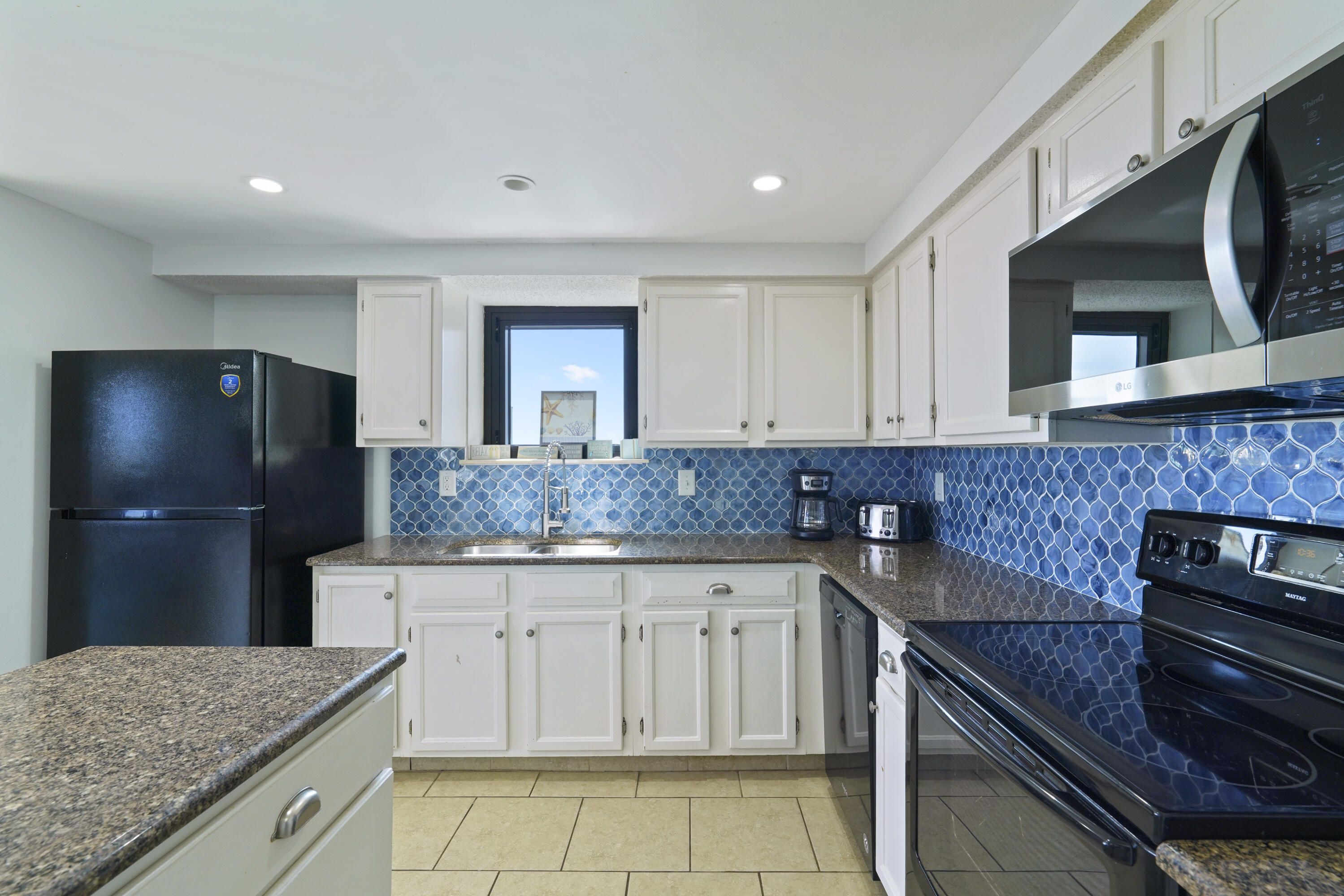 Kitchen with white cabinets, blue patterned tile backsplash, granite counters, and black appliances.
