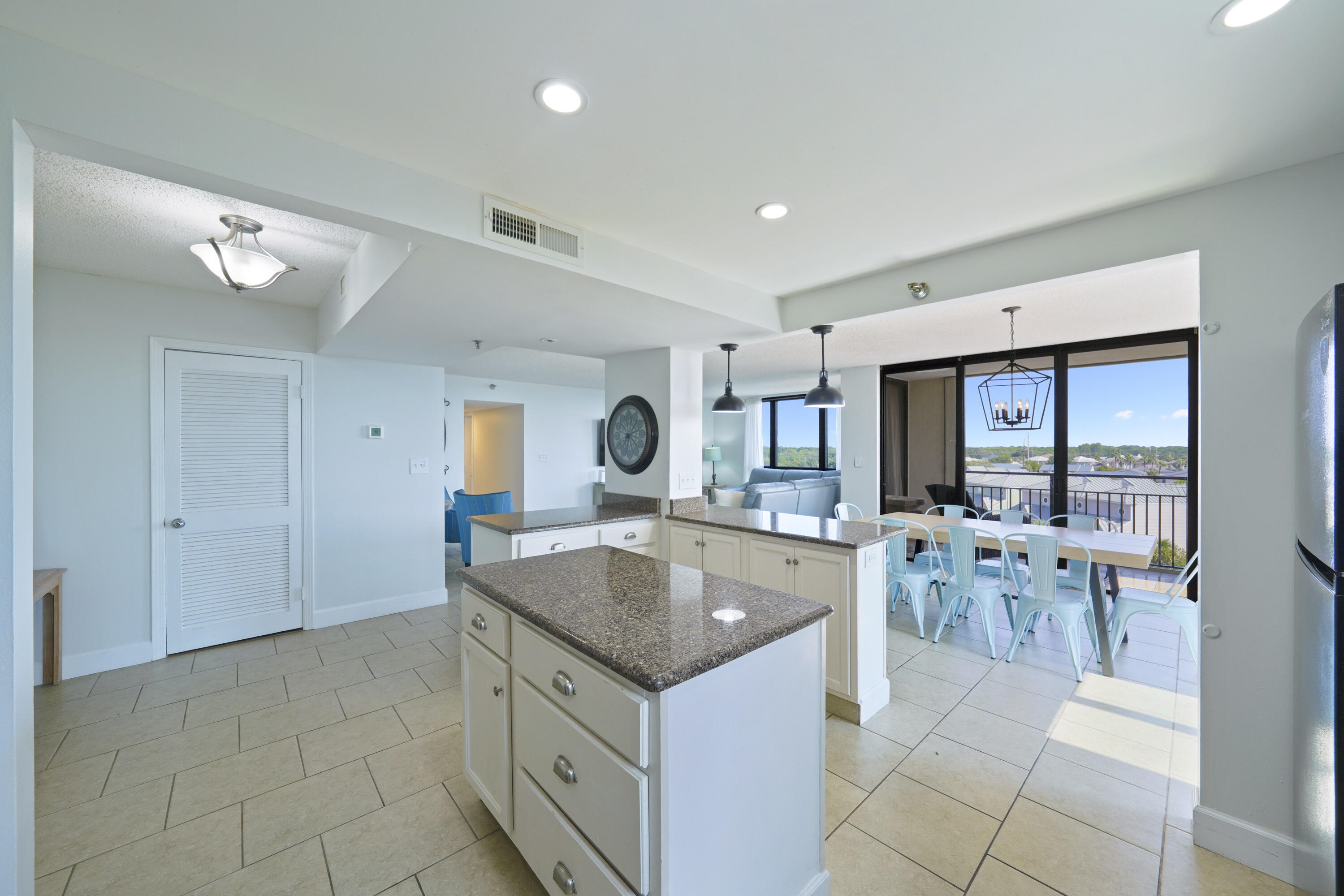 Open-plan condo kitchen with granite island and turquoise dining chairs beside a balcony with rooftop views.