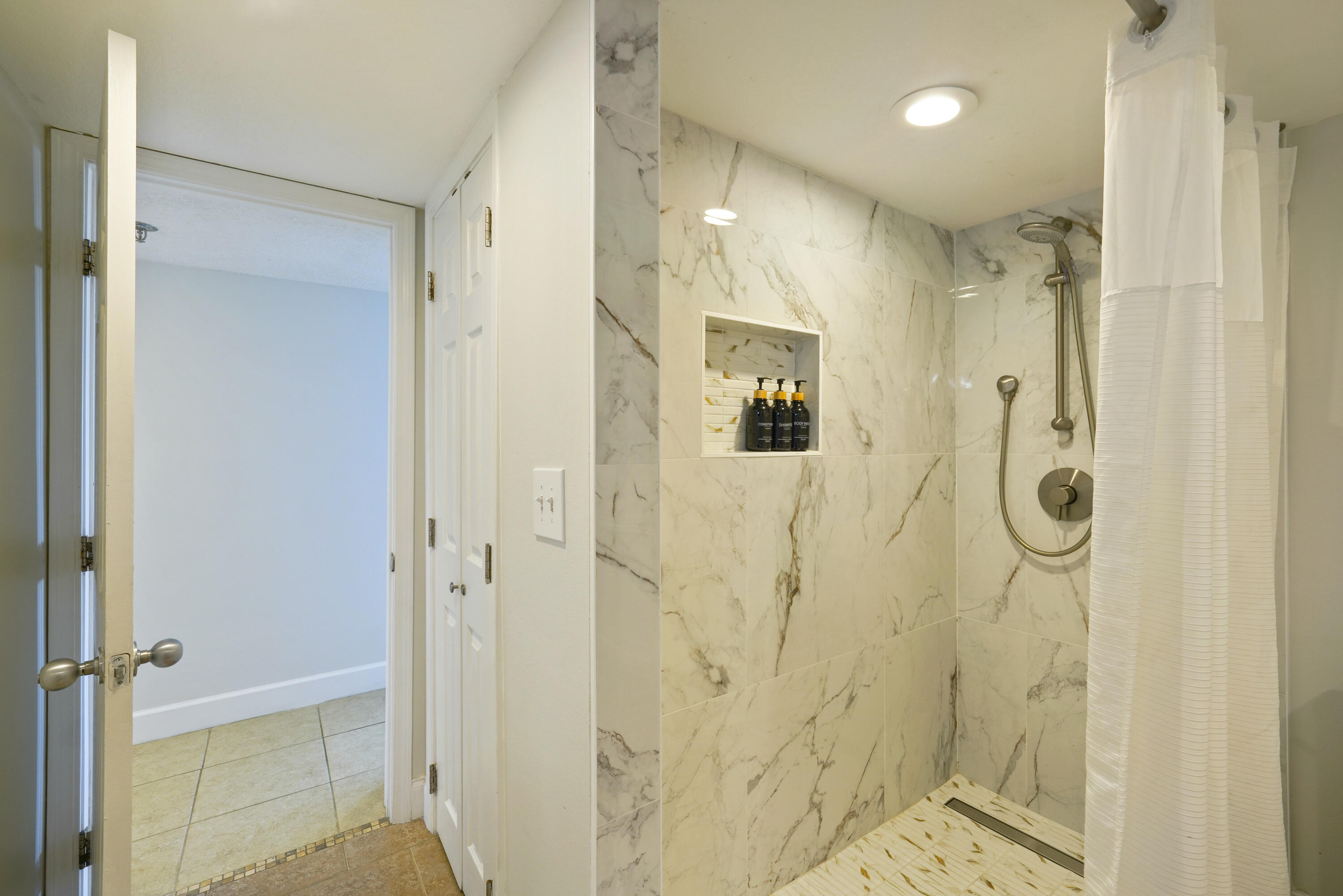 Walk-in shower with marble-look tile, recessed toiletry niche, and brushed-metal fixtures.