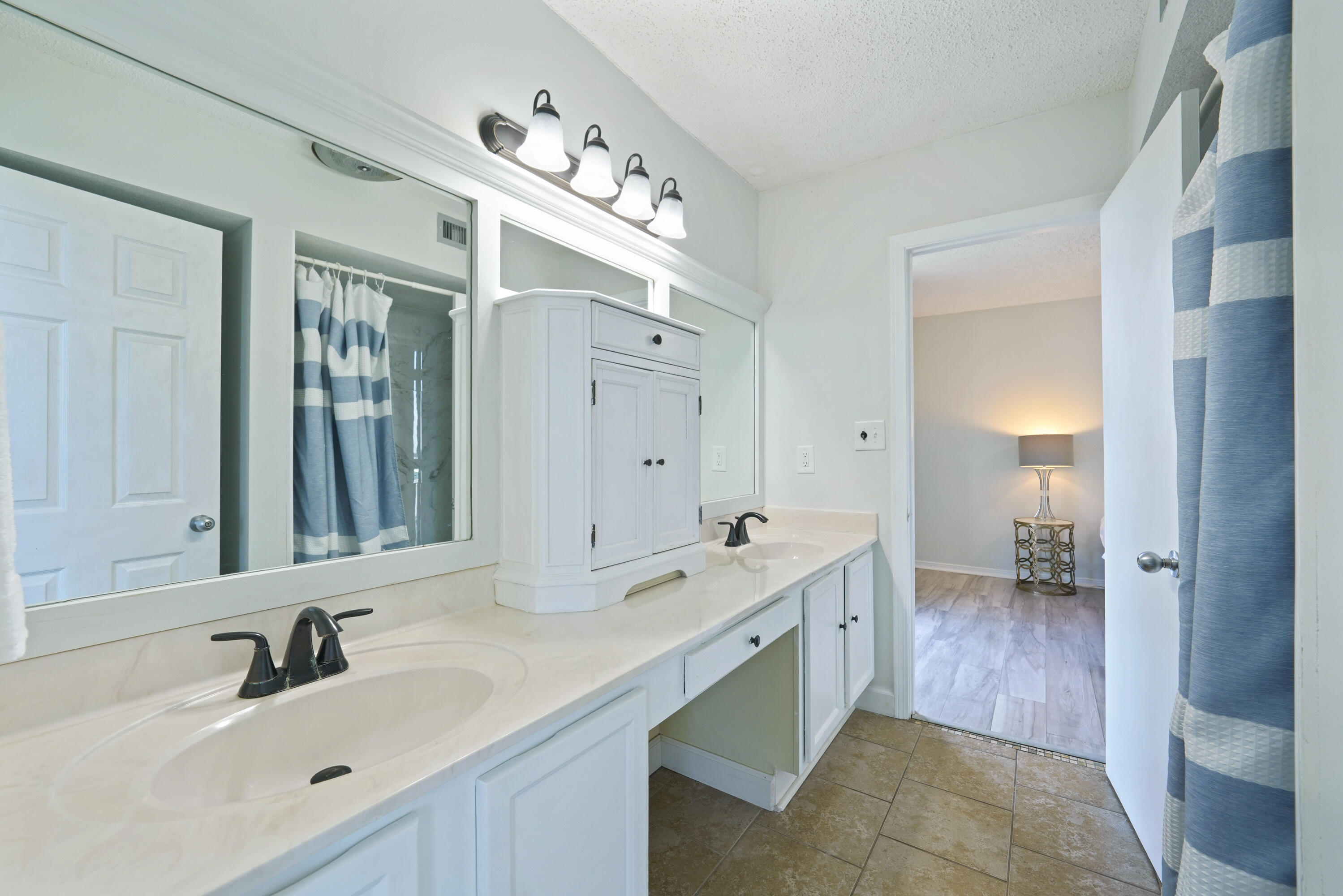 Bathroom with a long double-sink vanity, mirrored cabinets, and blue-and-white striped shower curtains.