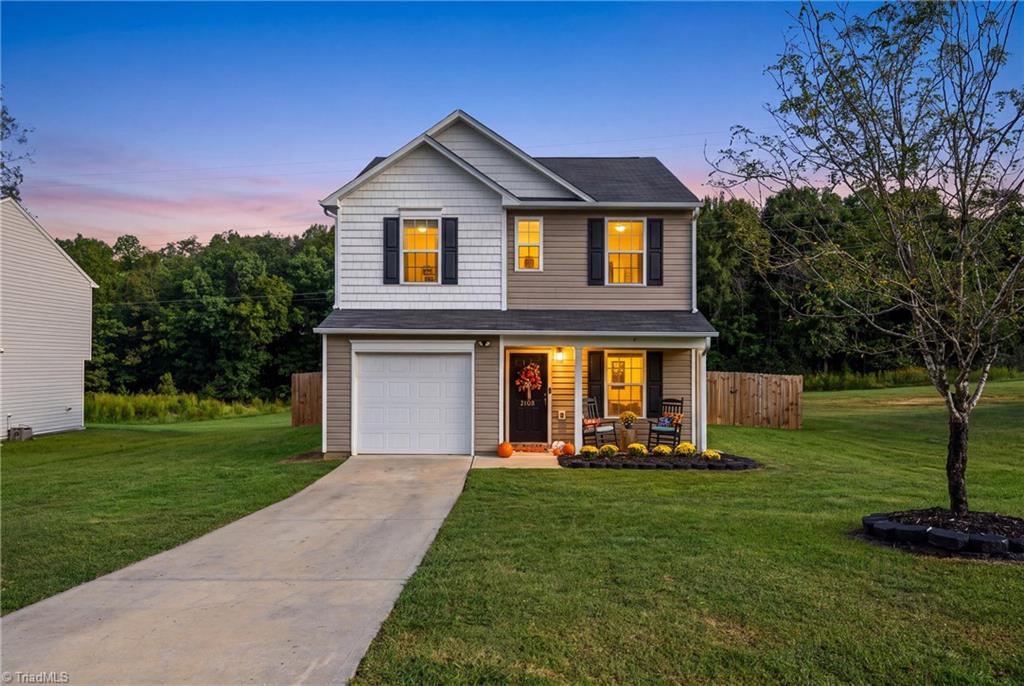 Two-story house with a covered porch, single-car garage, and warmly lit windows at dusk.