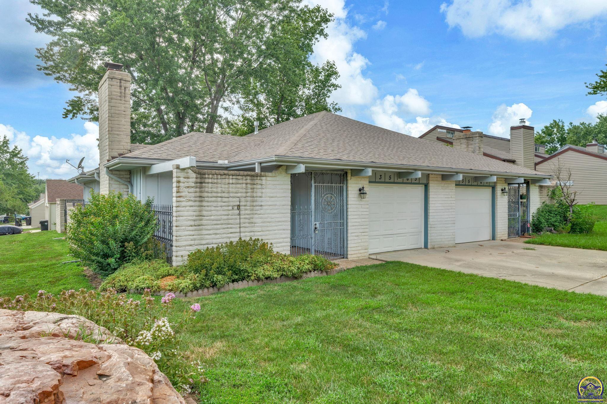 Stone residence with two garage doors, a gated front entry, and landscaped lawn.
