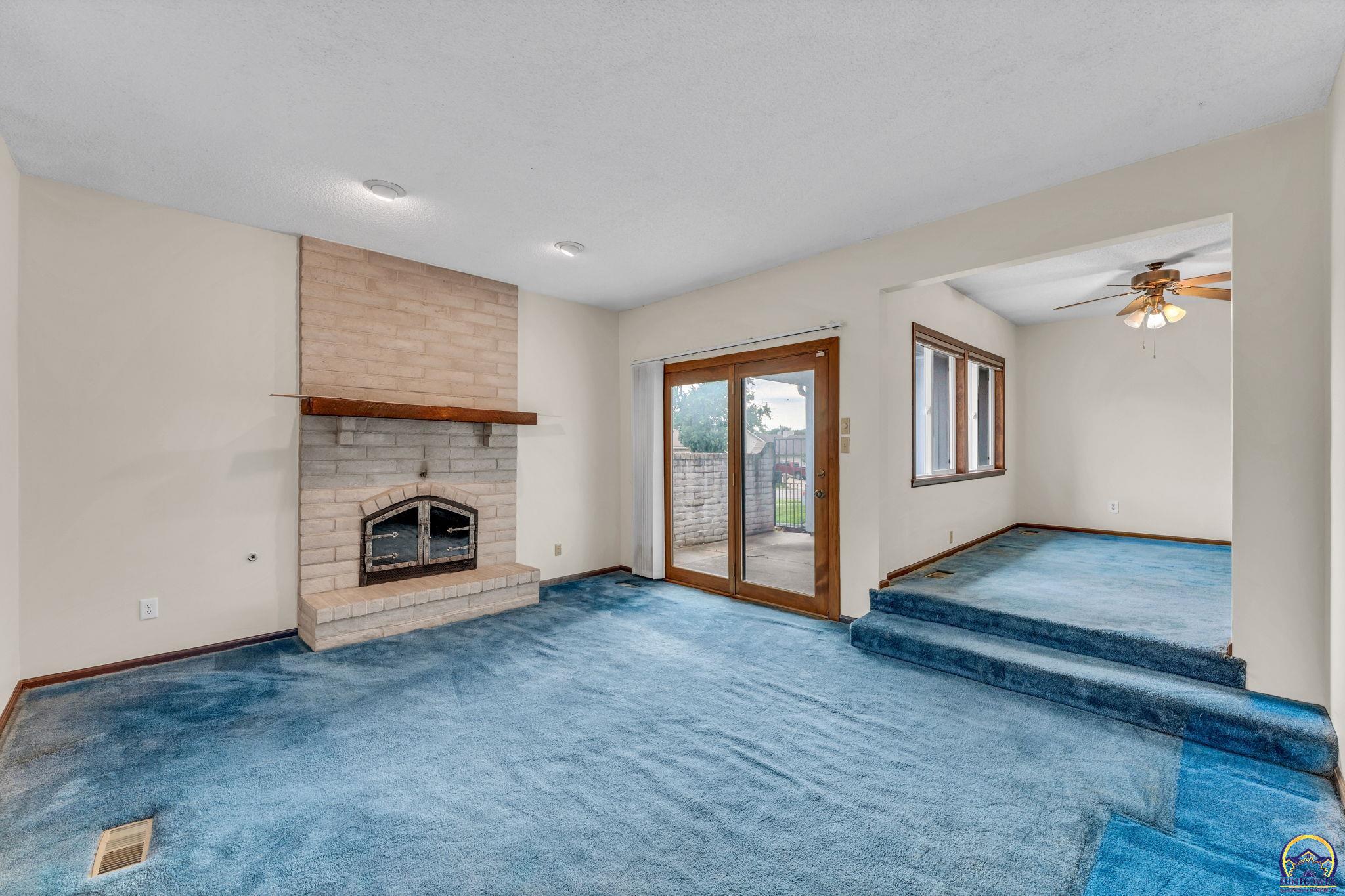 Living room with a brick fireplace, blue carpet, and sliding glass doors to a patio.