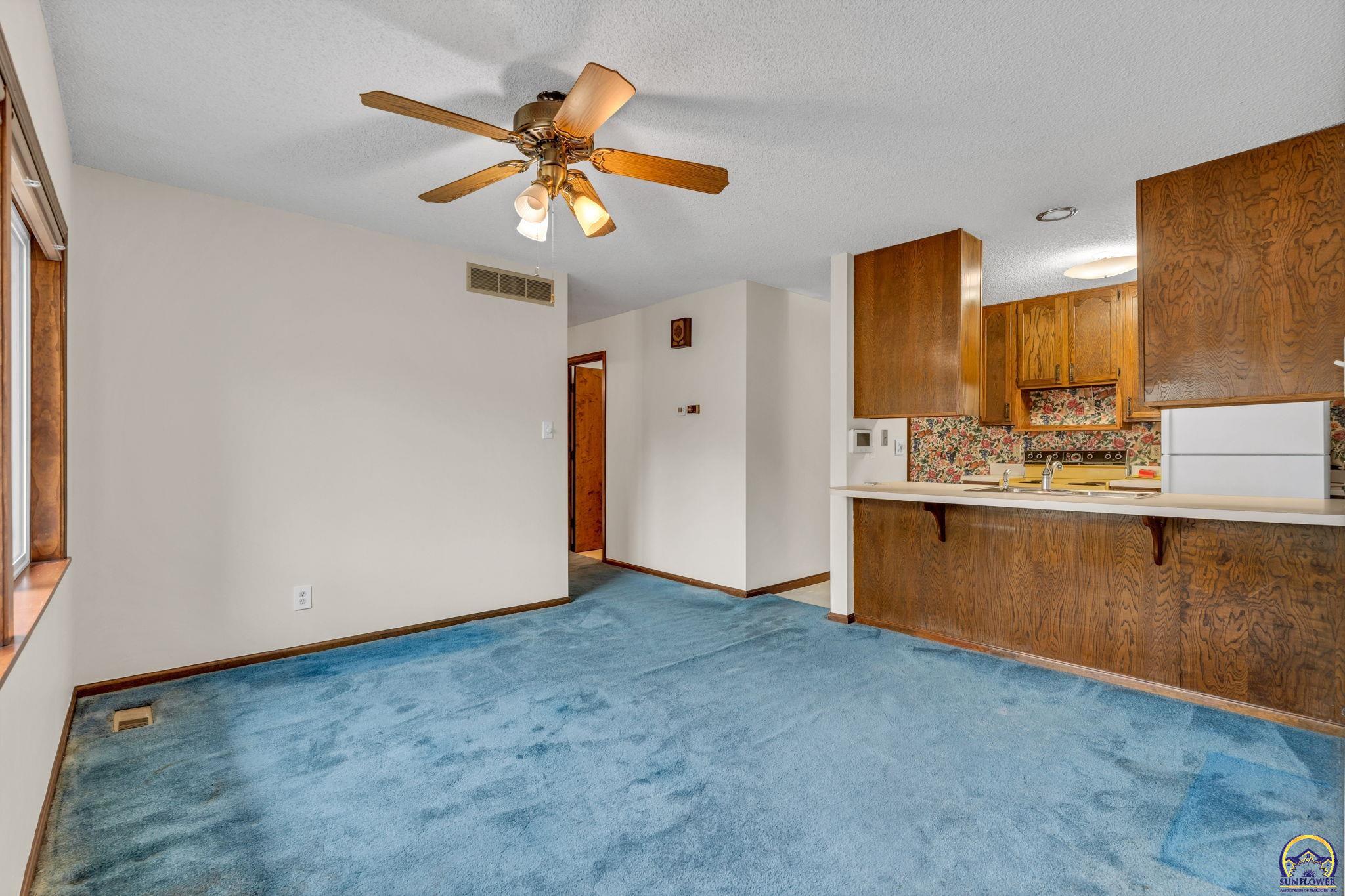 Blue-carpeted dining area opening to a wood-cabinet kitchen with a floral backsplash.