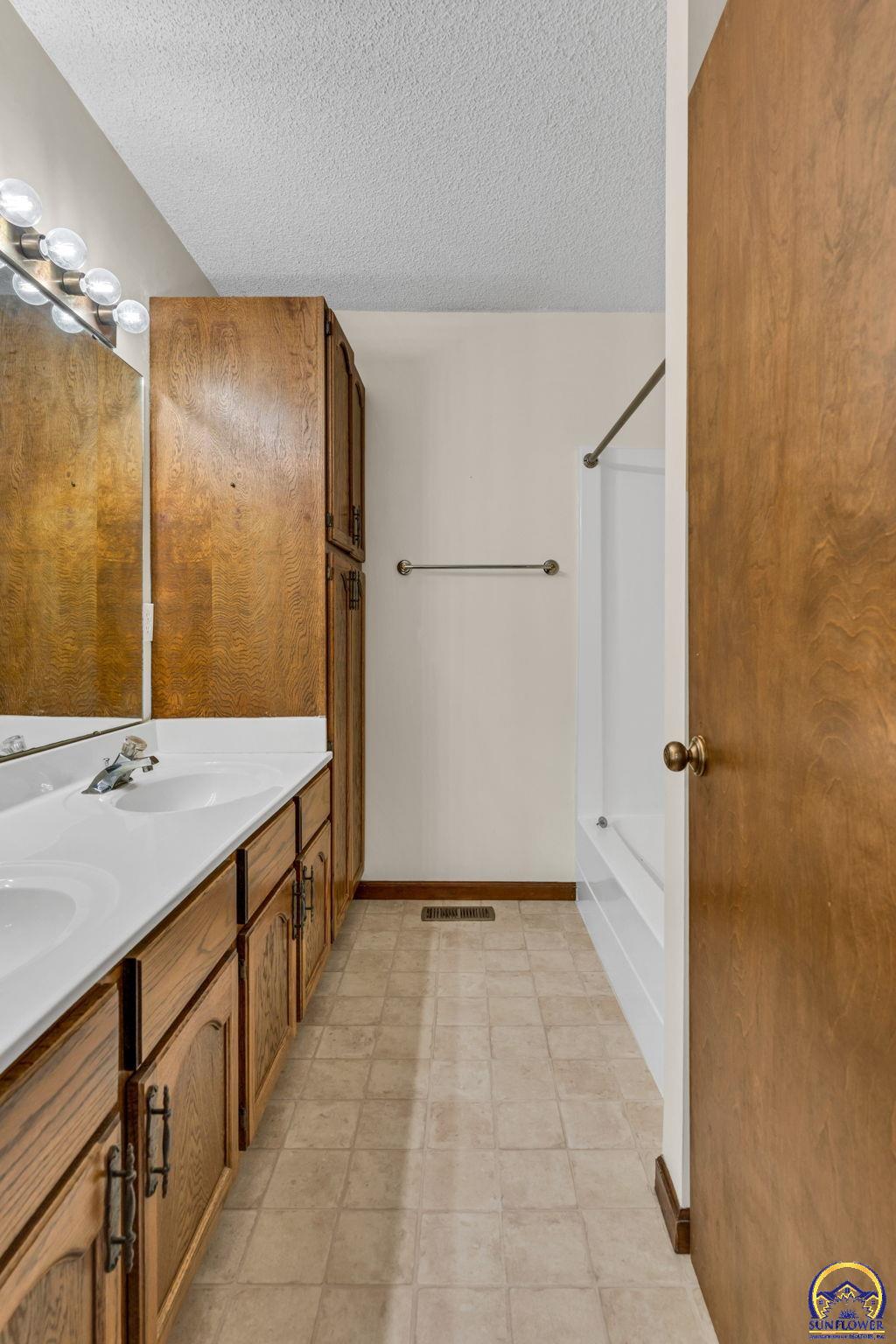 Bathroom with a long wood vanity, double sinks, tiled floor, and bathtub.