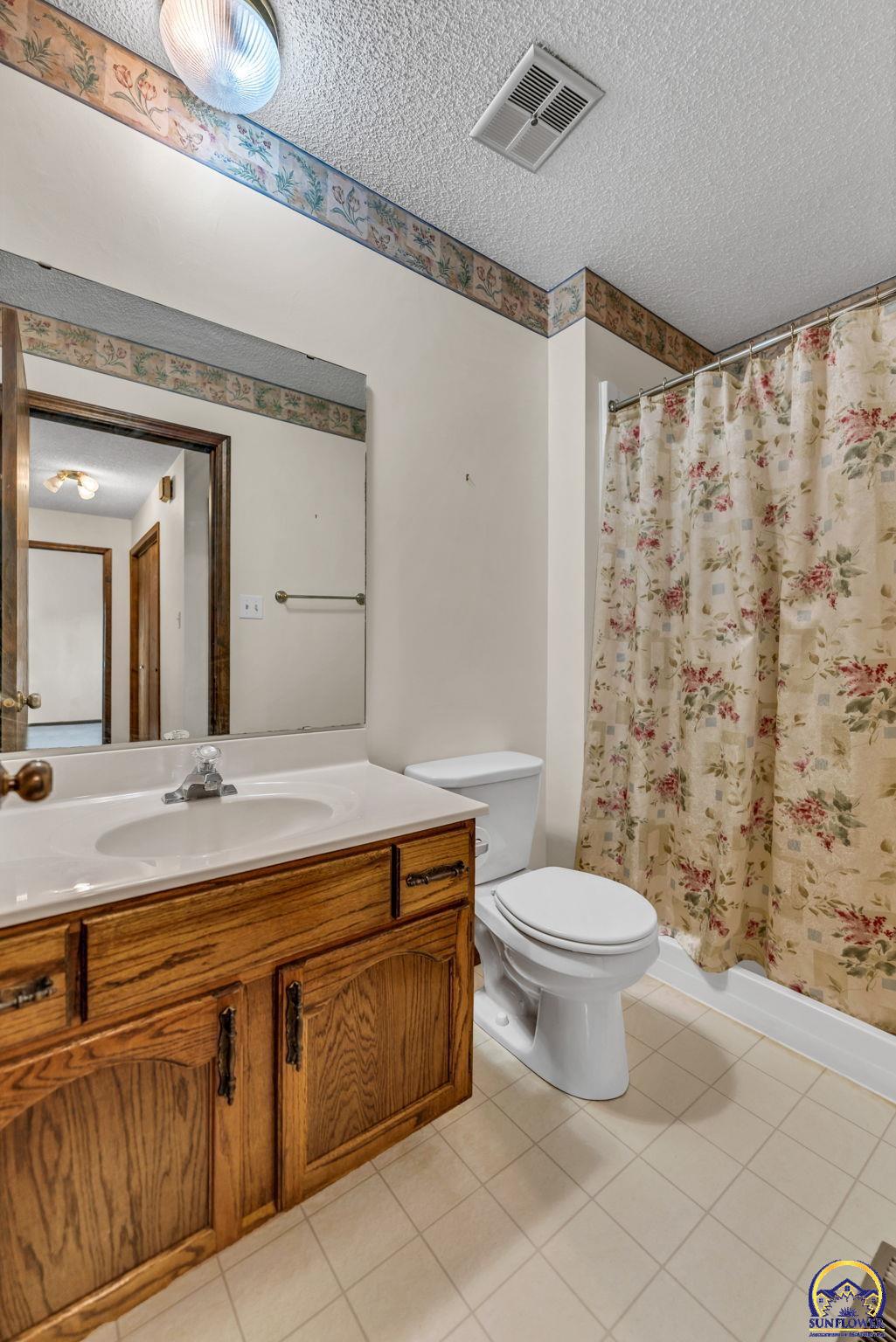 Bathroom with oak vanity, white sink and toilet, and a floral shower curtain.
