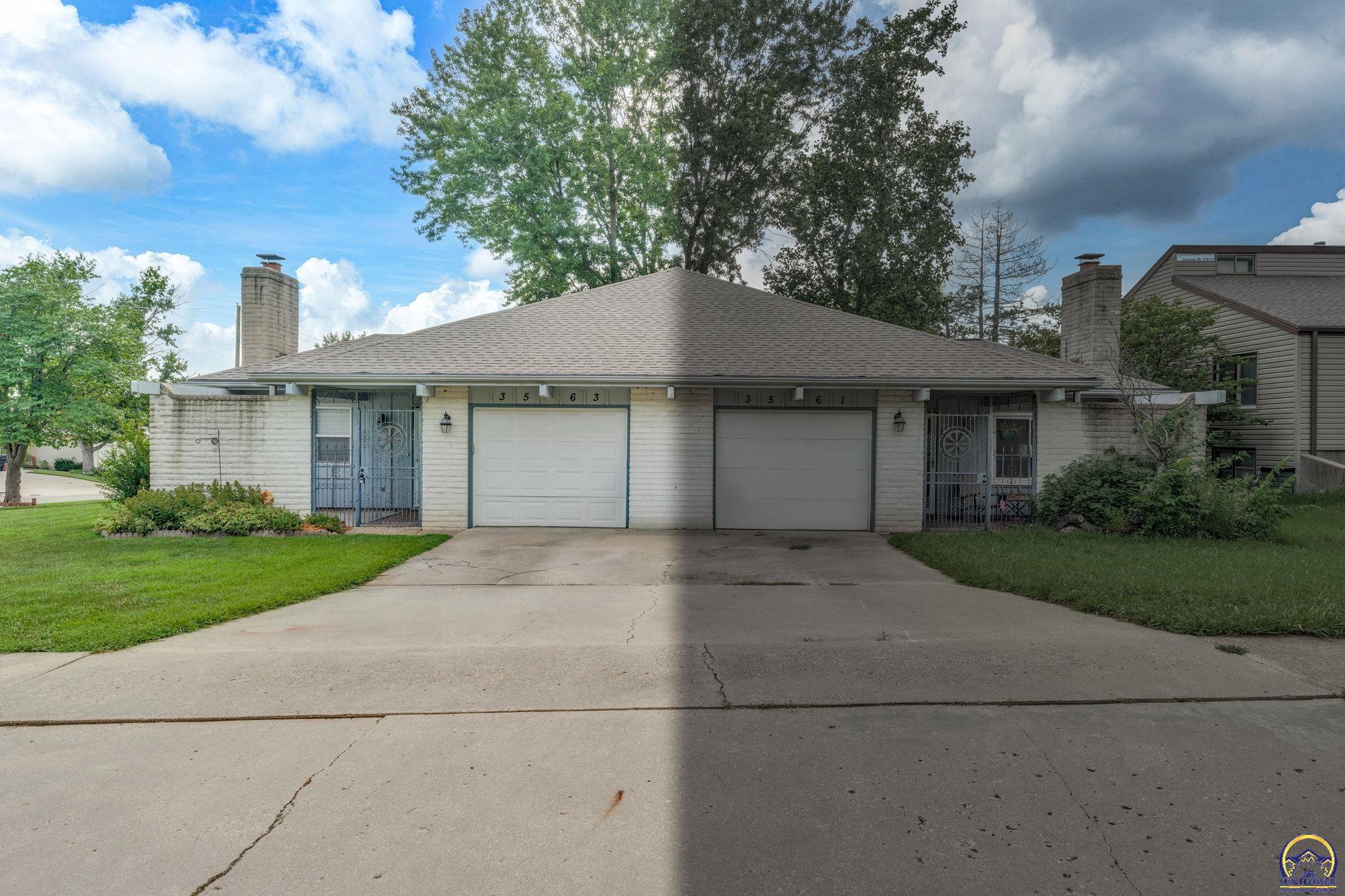 Light brick duplex with two garage doors, gated entrances, and a wide concrete driveway.