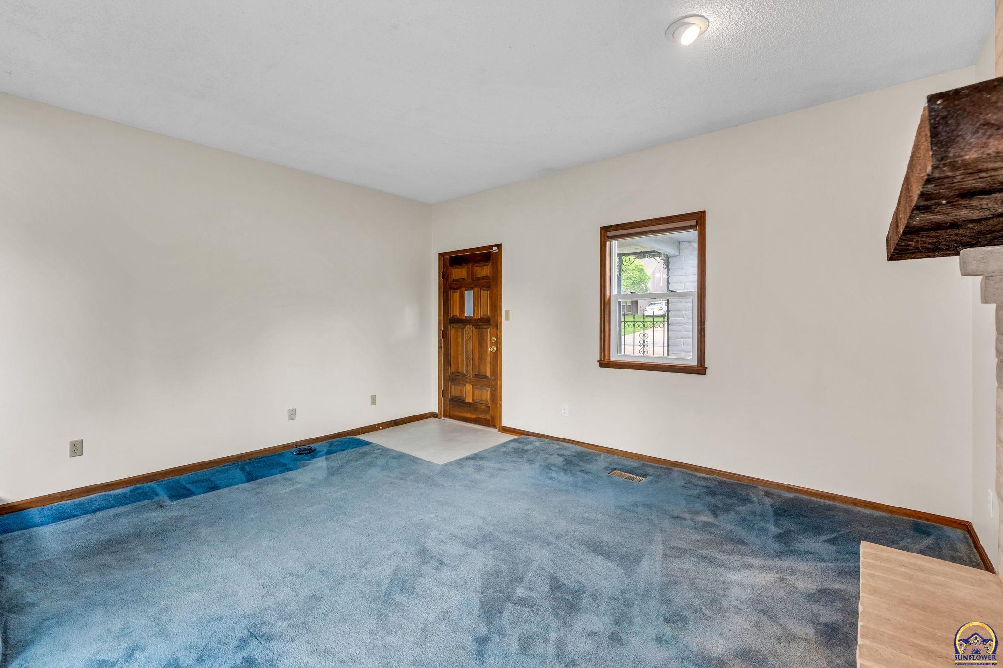 Empty living room with blue carpet, a wood entry door, and a window.