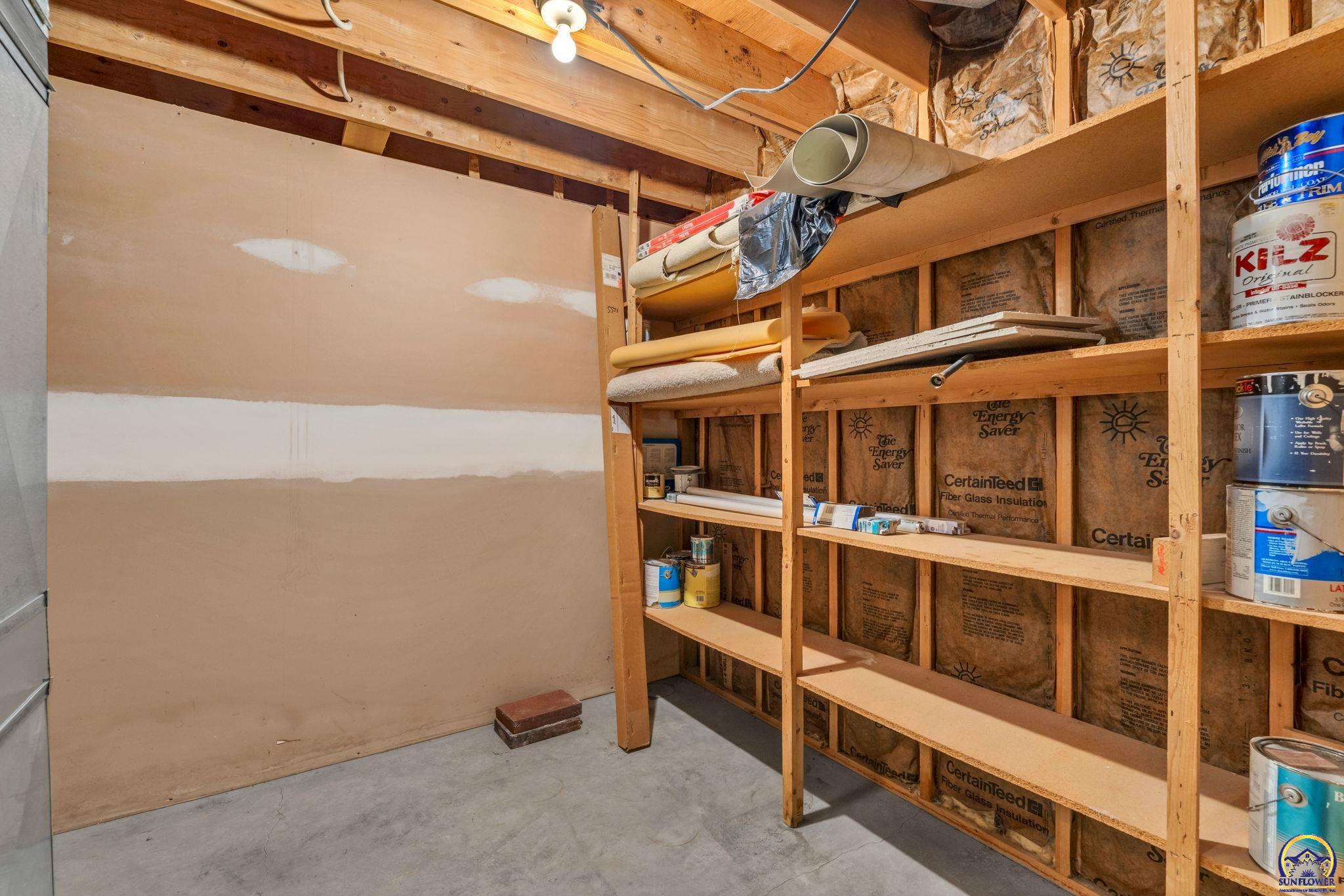 Unfinished basement storage area with exposed insulation and built-in wooden shelves.