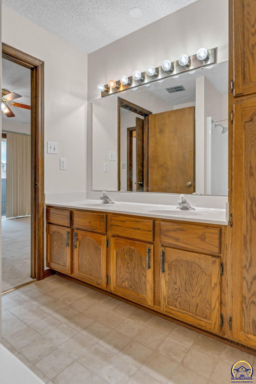 Bathroom vanity with two sinks, oak cabinetry, a large mirror and a row of lights.