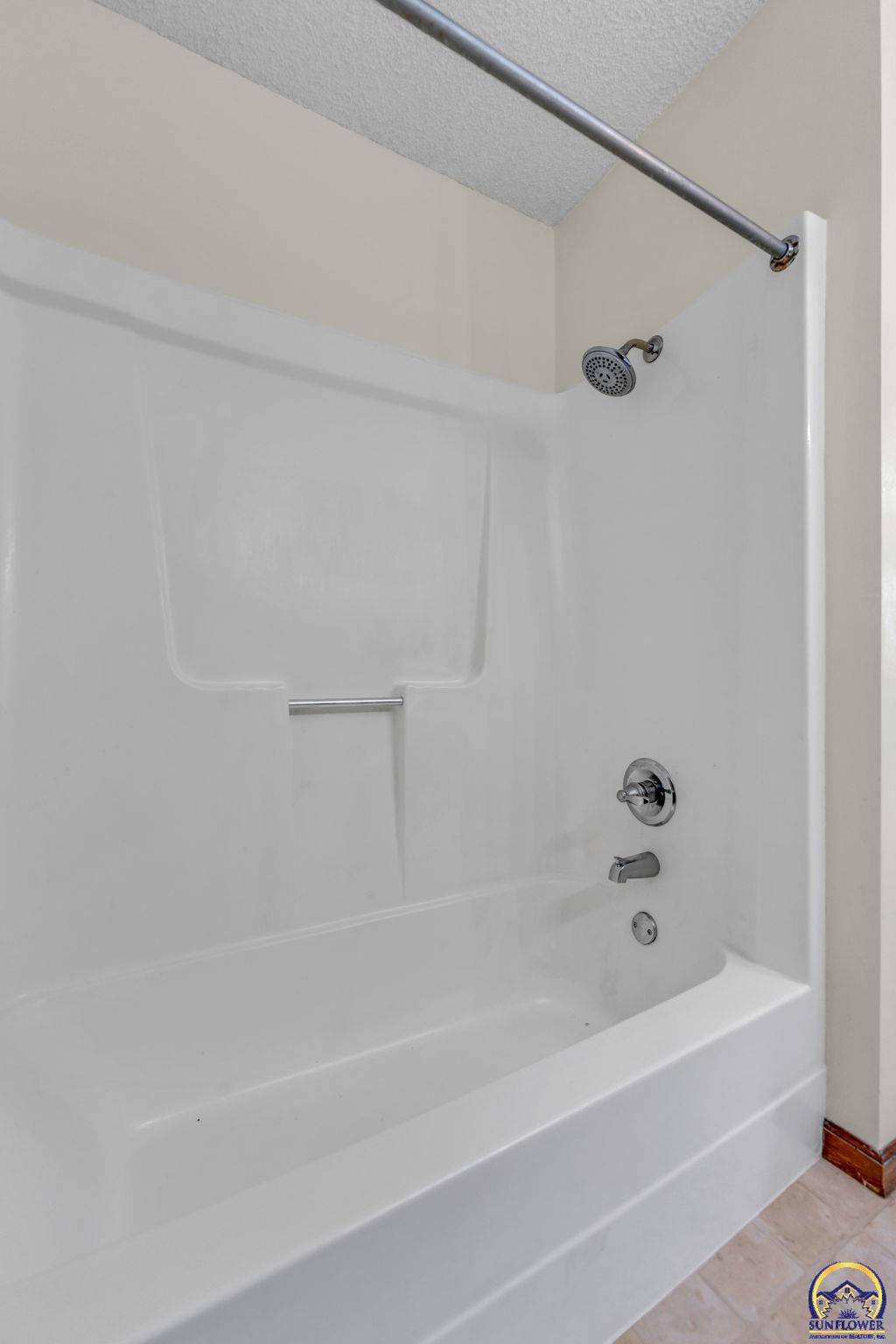 Bathroom with a white bathtub and shower surround, chrome fixtures, and a curtain rod.