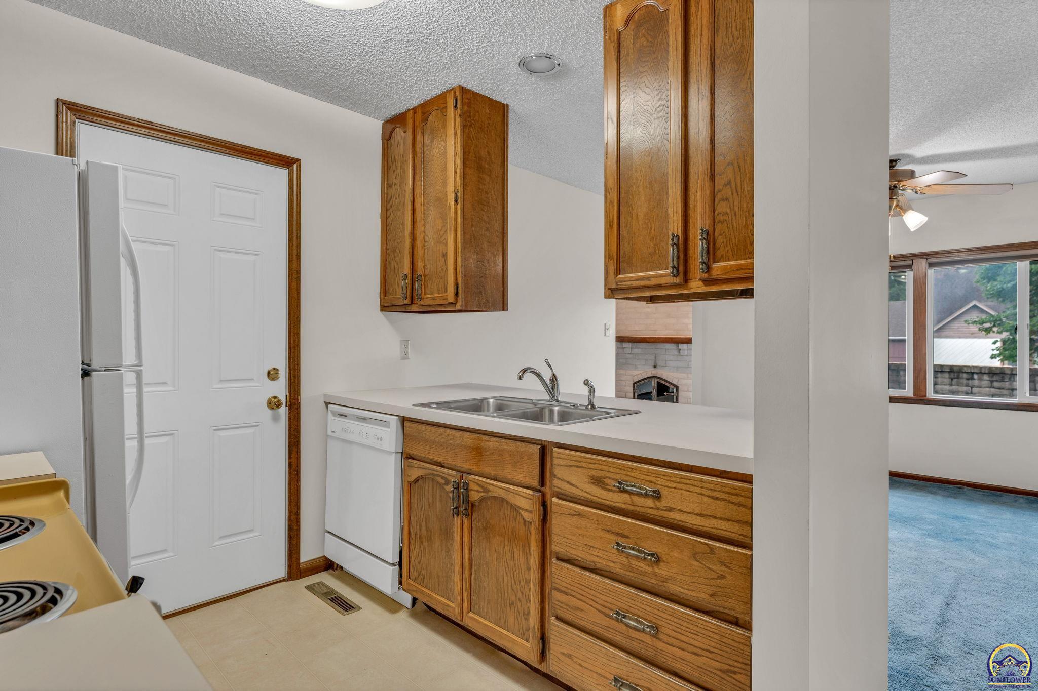 Kitchen with oak cabinets, a double-basin sink, white appliances, and a pass-through to the adjoining room.