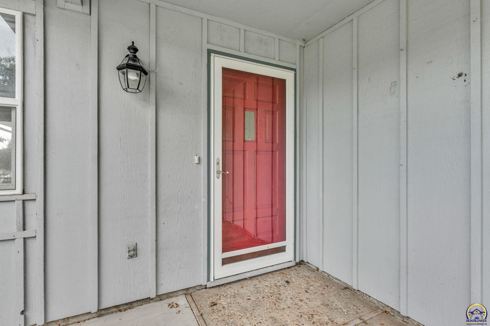 Covered home entry with a red screened front door and black wall lantern.