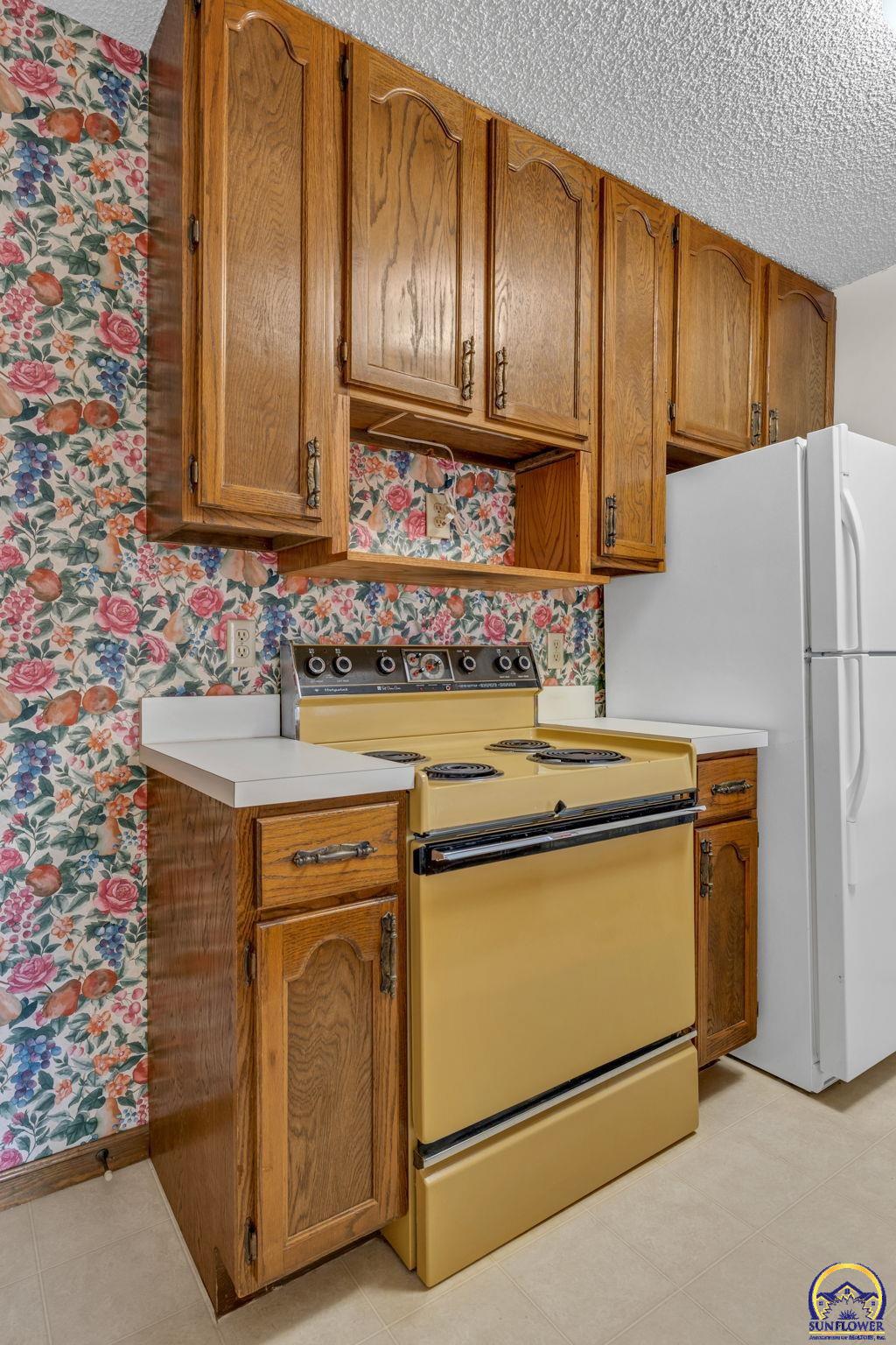 Kitchen with oak cabinets, floral wallpaper, and a vintage yellow electric range.