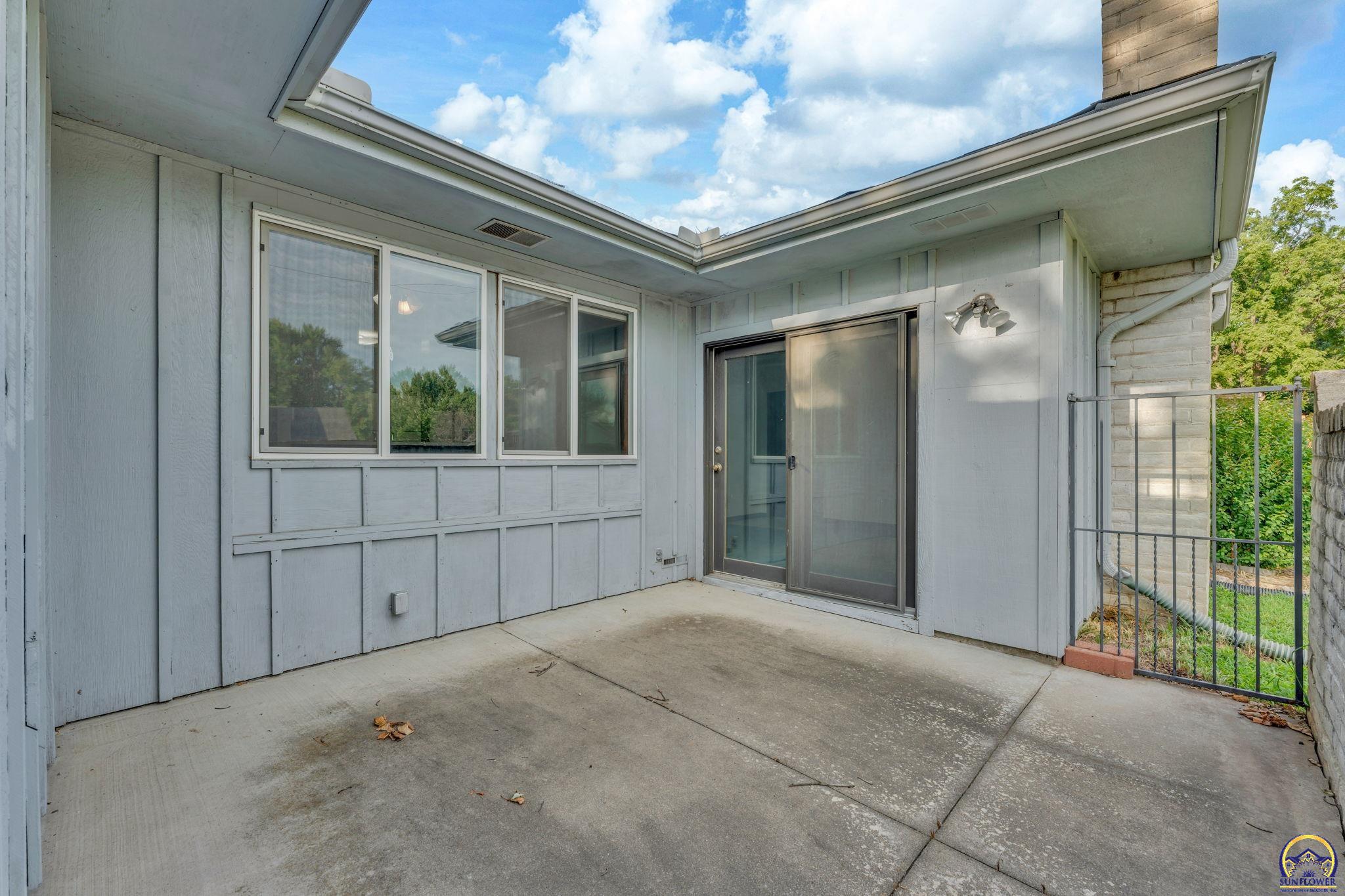 Covered concrete patio with wide windows, a sliding glass door, and a metal side gate.