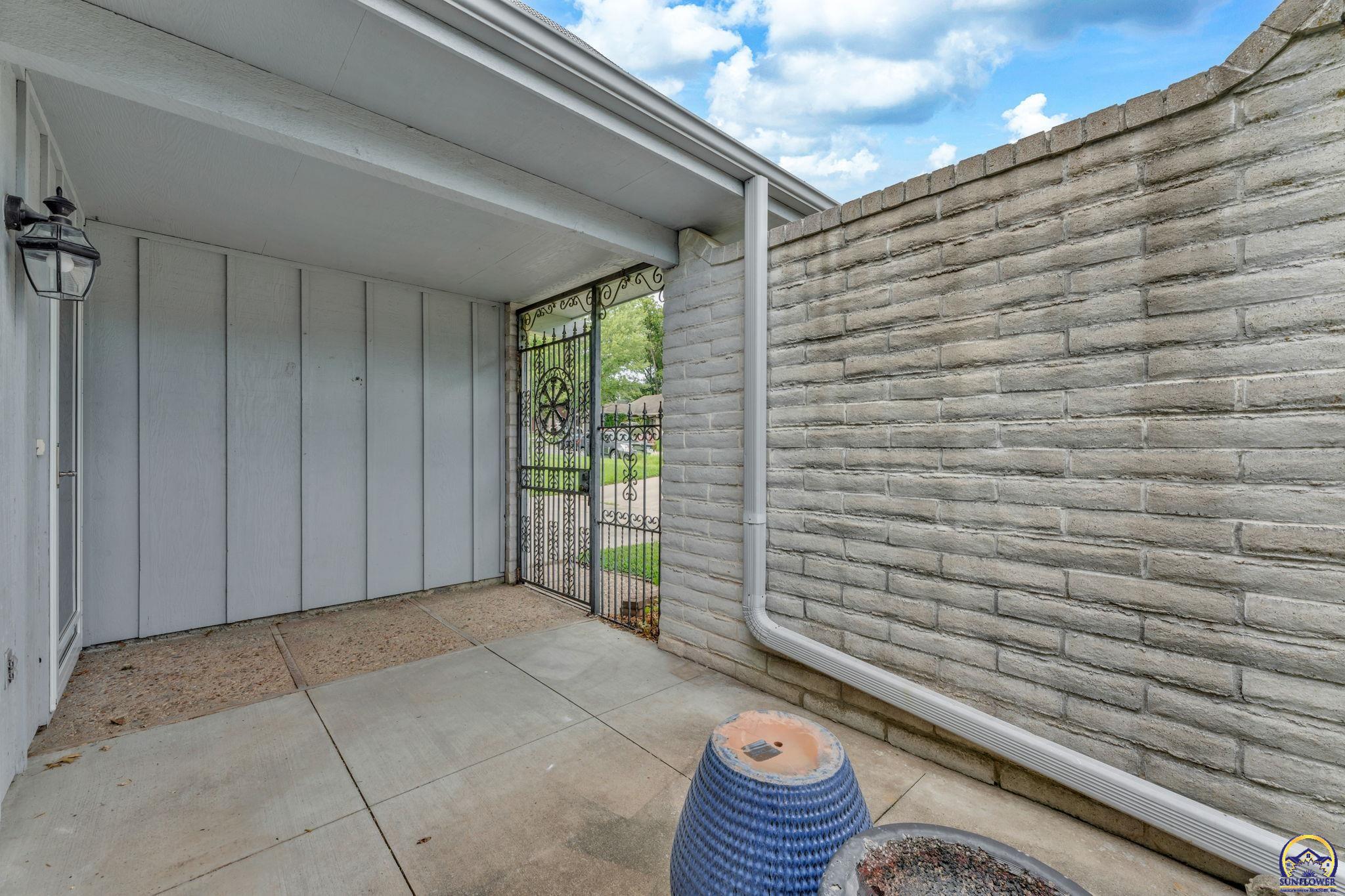 Covered patio with a wrought-iron gate and tall stone privacy wall.