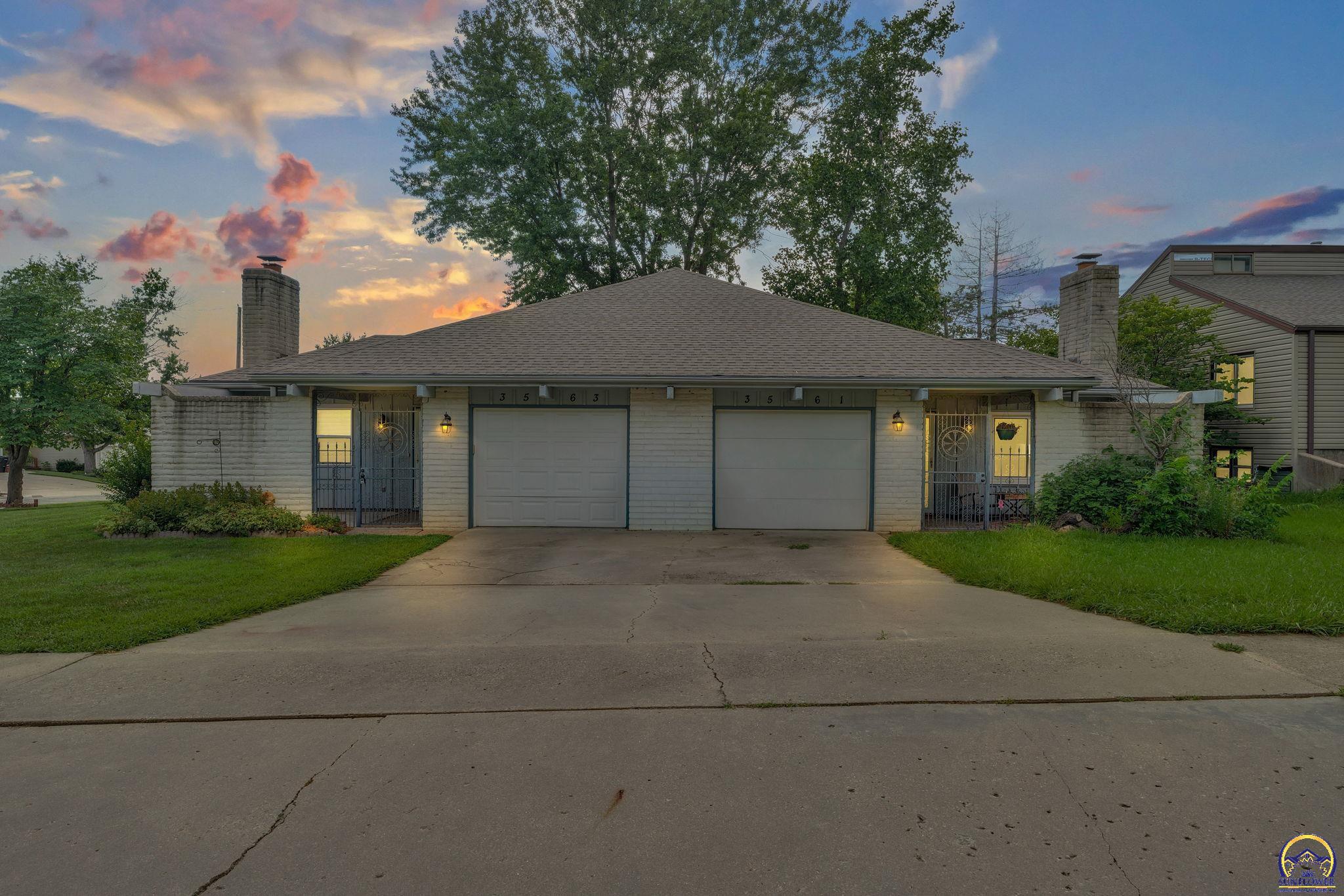 Stone-faced duplex with two garage doors and separate entrances at dusk.