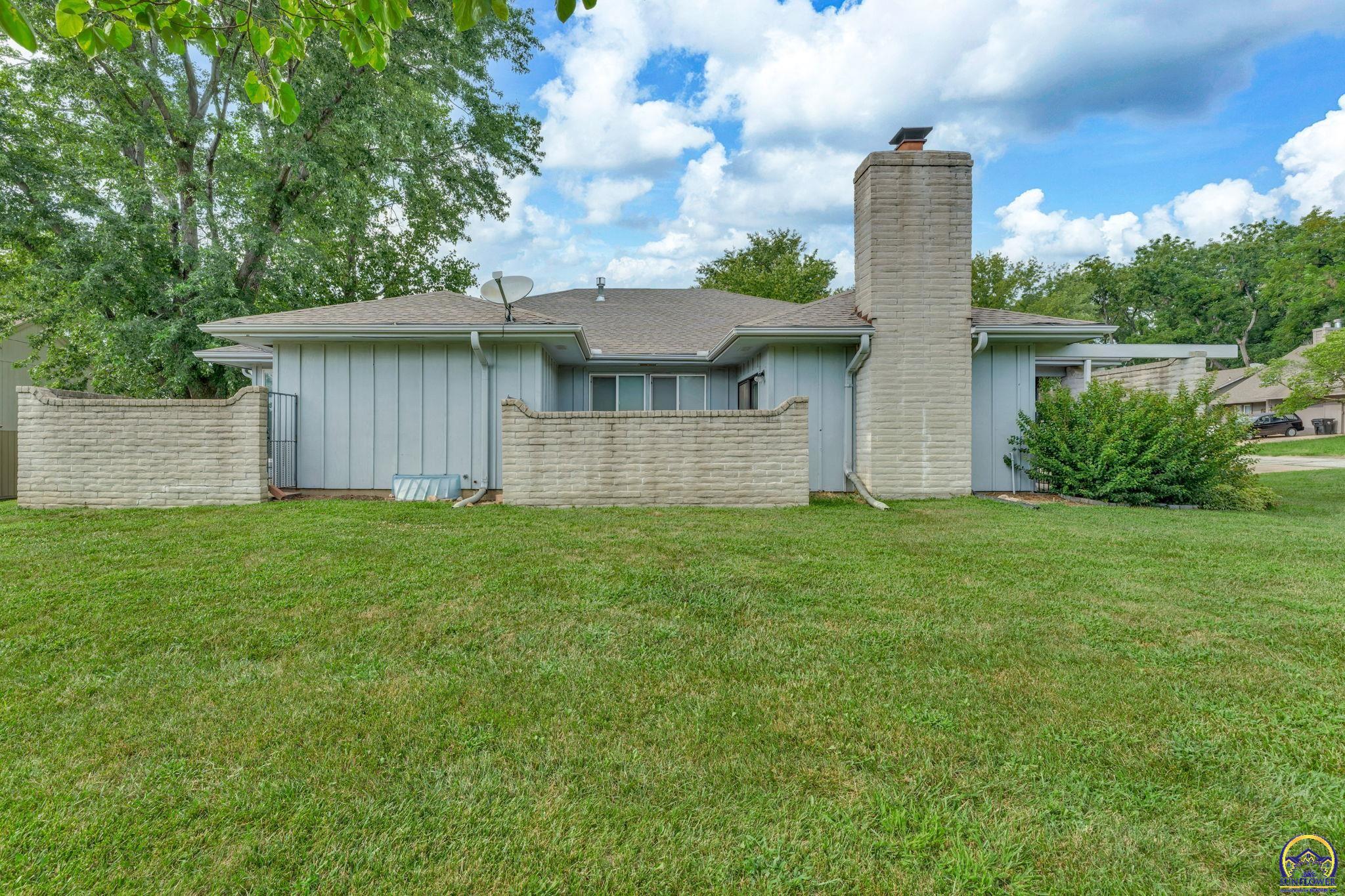 Rear of a home with a tall stone chimney, low stone walls, and green lawn.